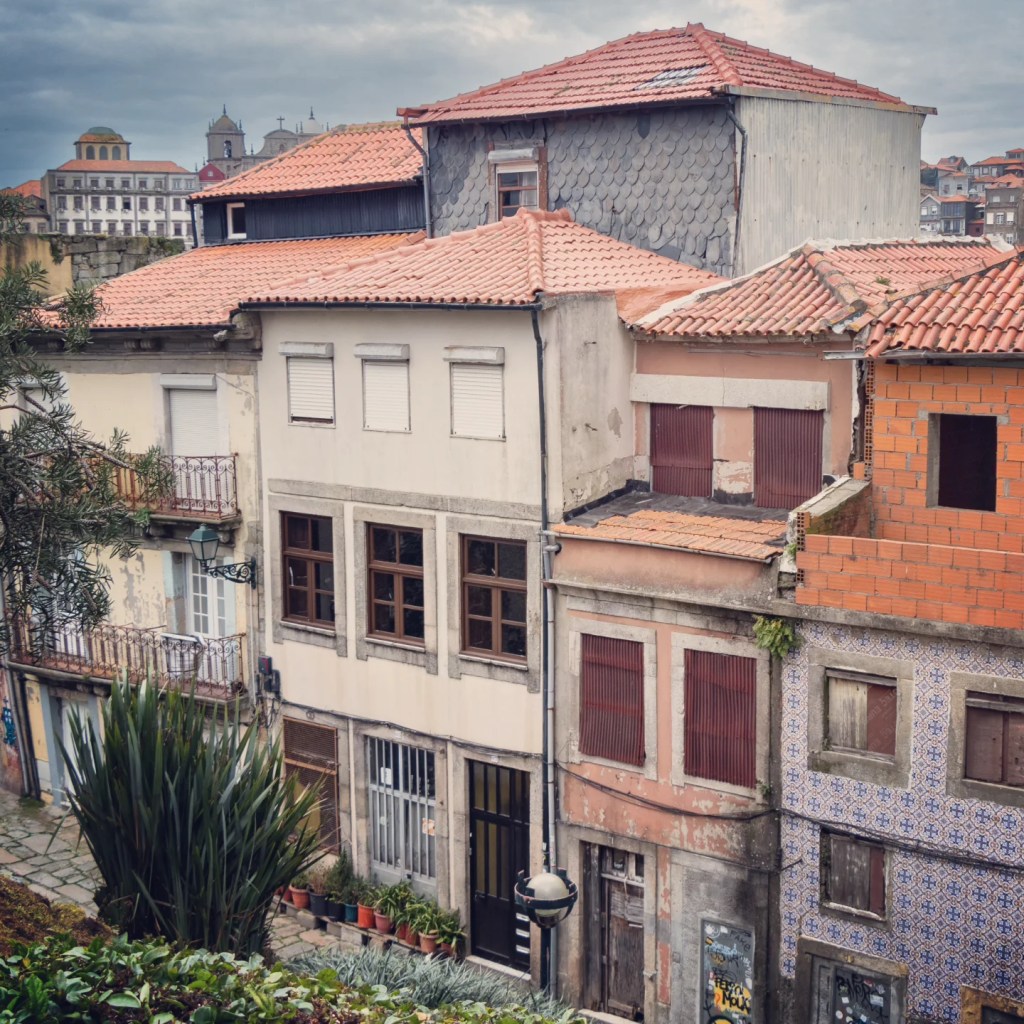 View over red-tiled residential rooftops in Porto, with a mix of painted facades and exposed brickwork, and church towers visible in the distance.