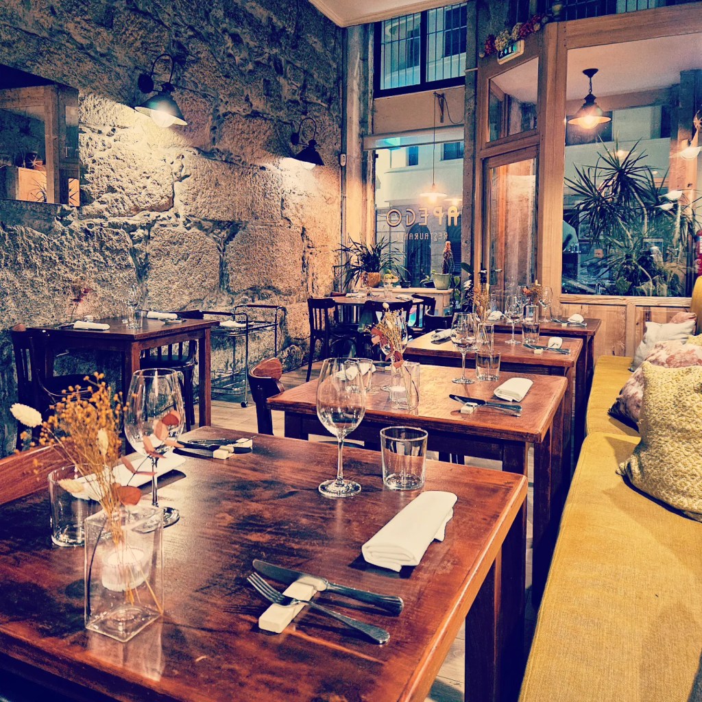 Cozy dining space at Apego Restaurant in Porto, featuring stone walls, wood tables, and soft lighting with wine glasses set for dinner.