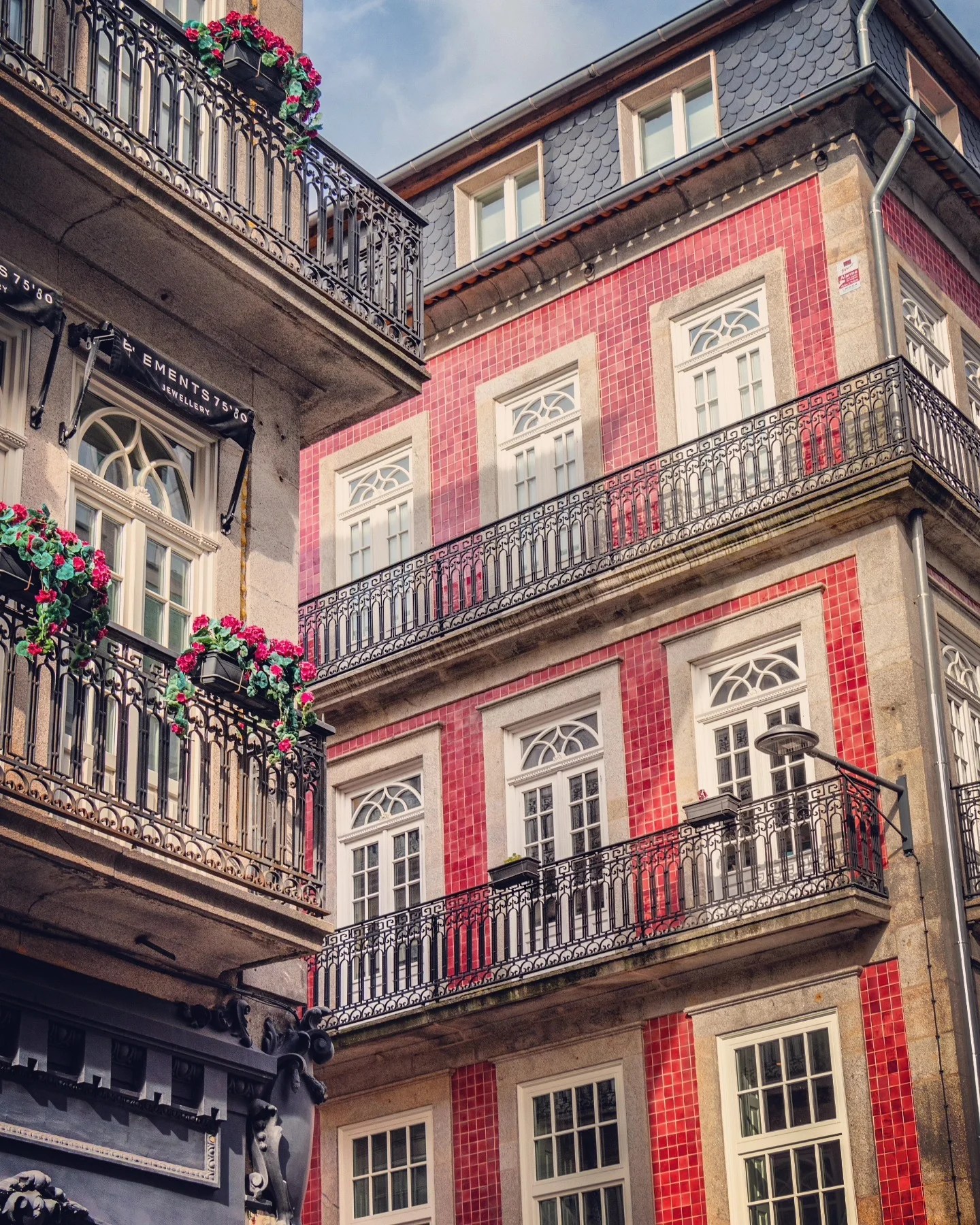 Traditional Porto buildings with red tiled façades and wrought-iron balconies decorated with flower boxes.