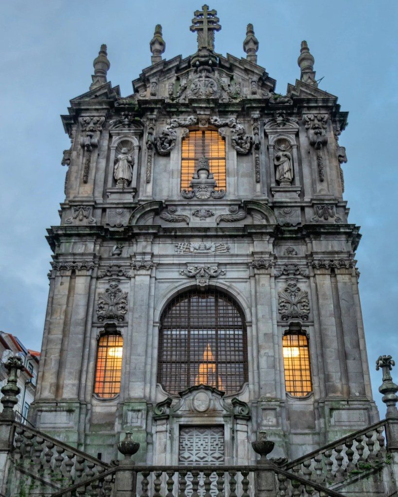 Close-up of the ornate stone façade of Igreja dos Clérigos in Porto, Portugal, illuminated with warm lighting against a twilight sky.
