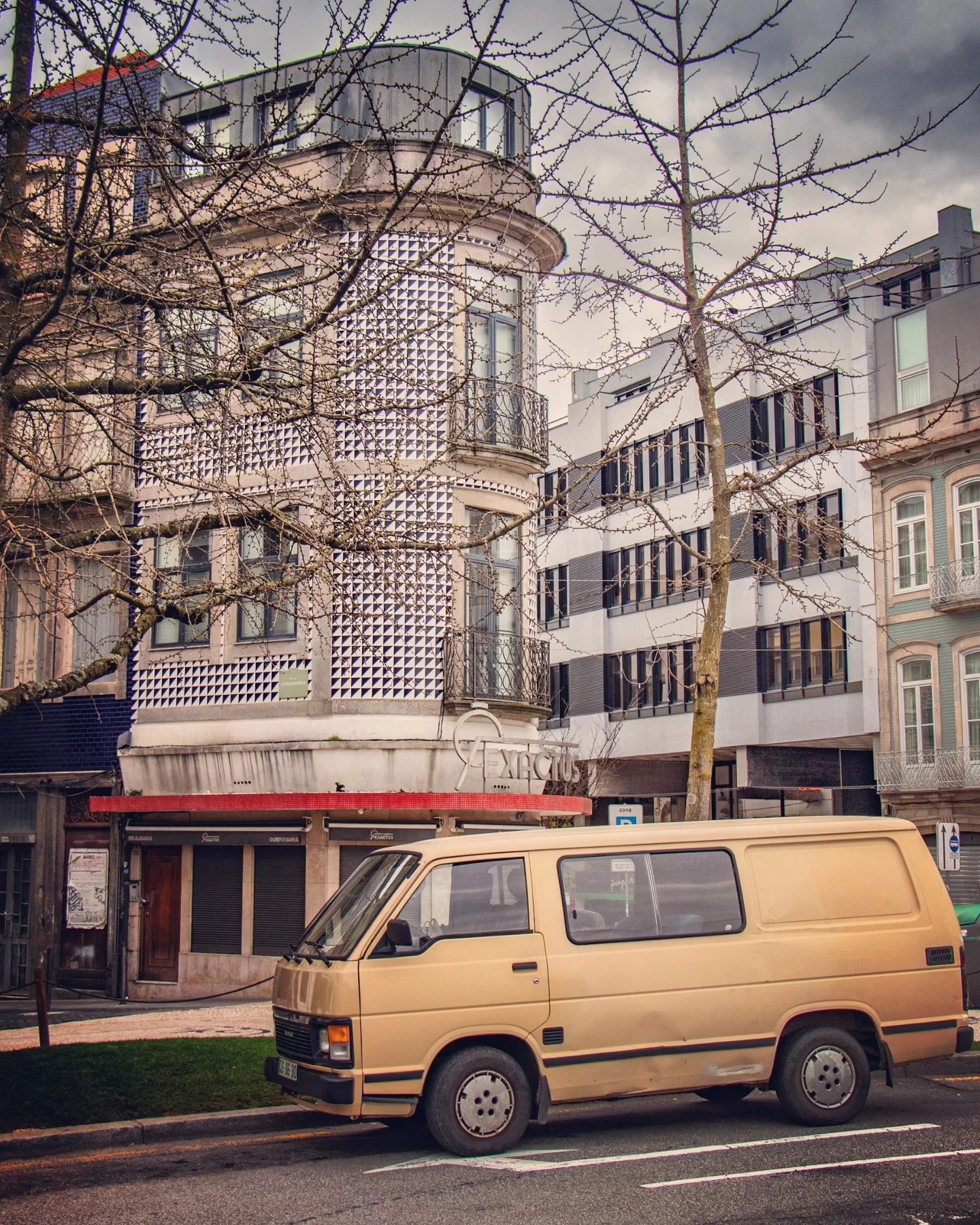 A beige vintage van parked on the street in front of a corner building decorated with a geometric black and white tiled facade in Porto.