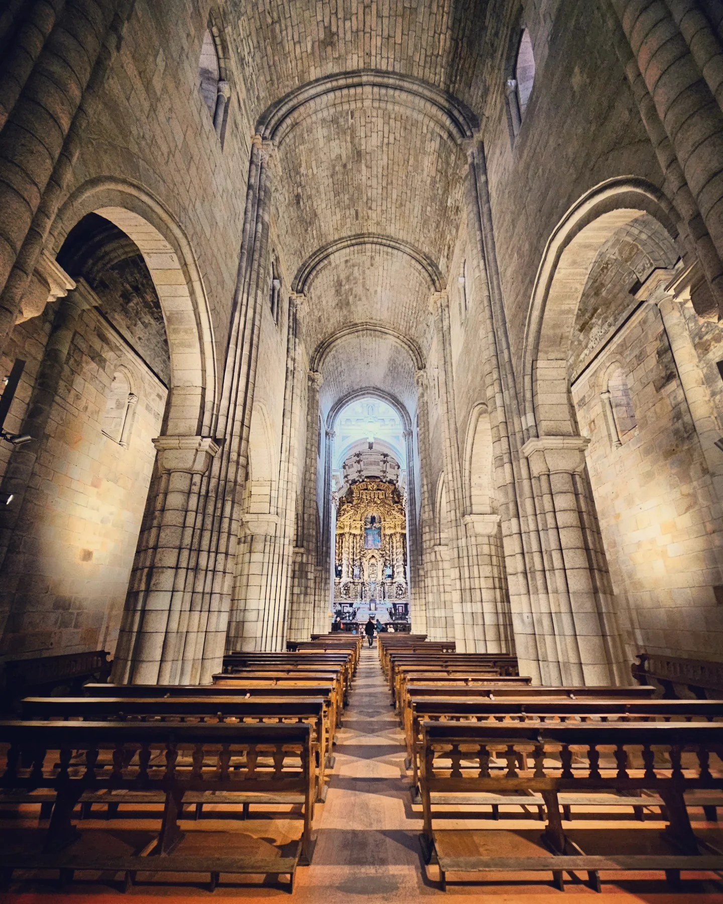 A view down the nave of Porto Cathedral, showing stone arches and vaulted ceilings leading to an ornate golden altar.