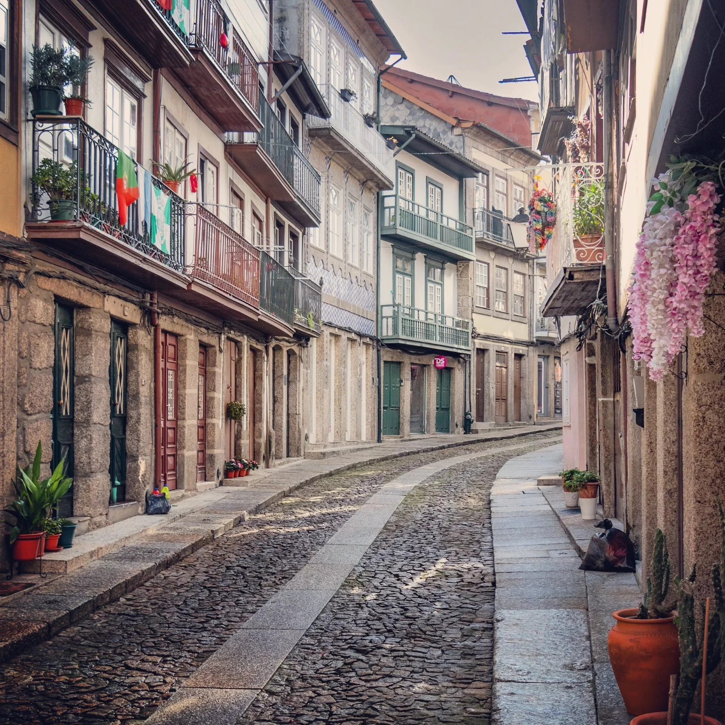 A curving cobblestone street lined with colorful traditional Portuguese houses with iron balconies and laundry hanging, in the historic center of Guimarães.