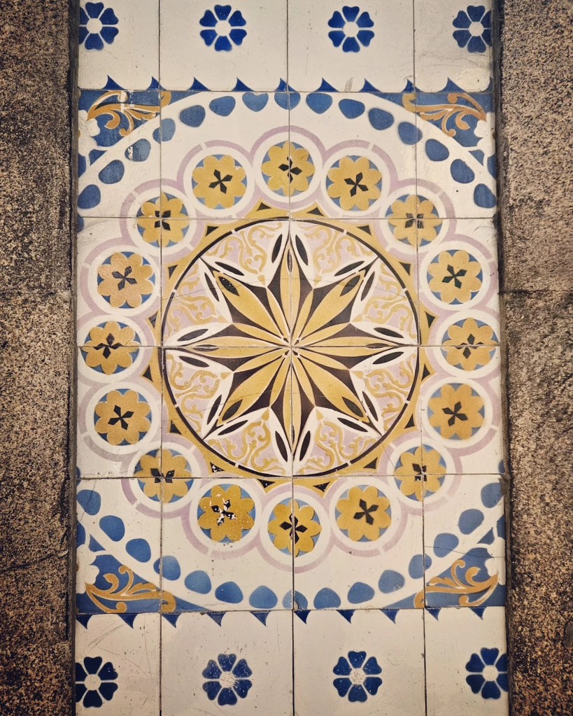 A close-up of a decorative azulejo wall tile at São Bento train station in Porto, featuring a yellow, blue, and white starburst and floral pattern.