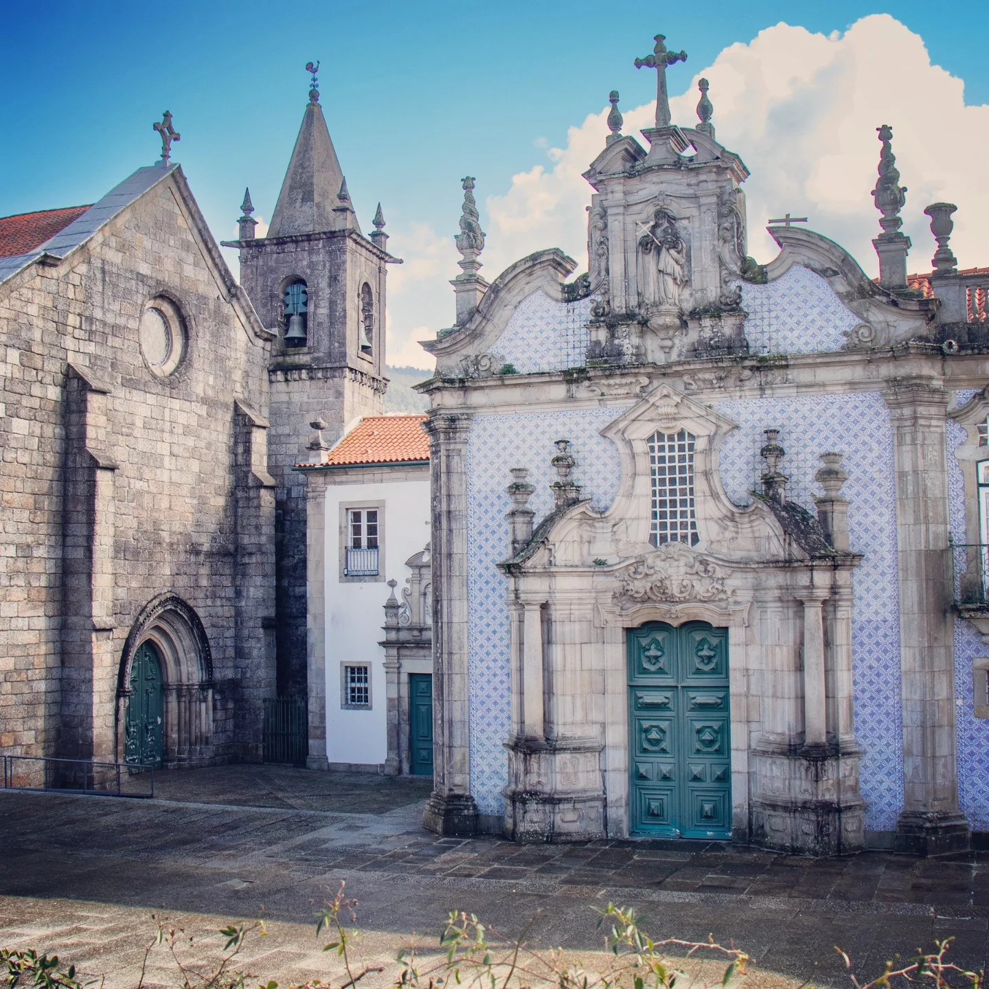 View of Igreja de São Francisco in Guimarães, Portugal, featuring its ornate Baroque blue and white tiled facade next to the adjoining Gothic stone convent building under a bright blue sky.