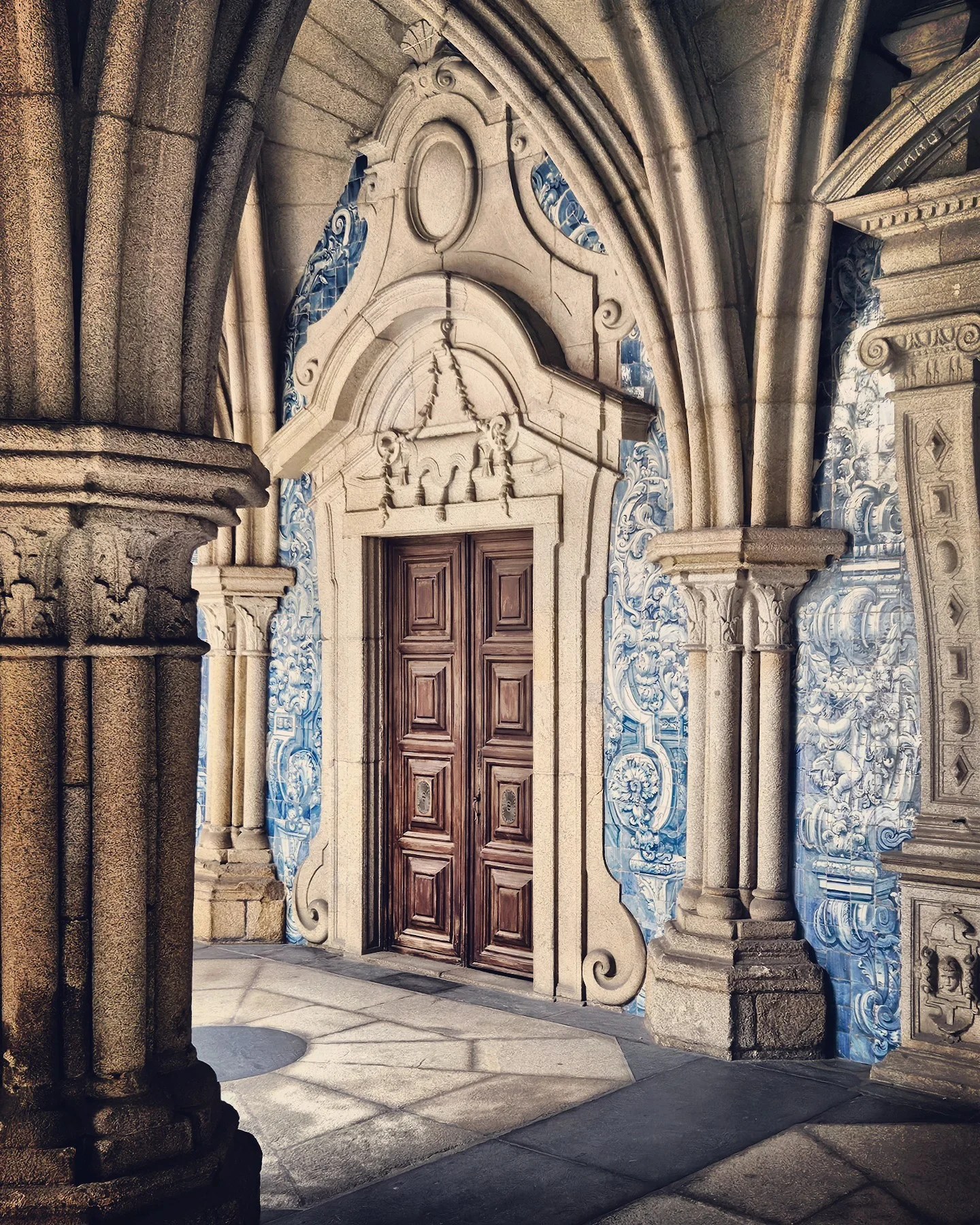 A wooden door framed by Gothic stone arches and surrounded by classic blue and white azulejo tiles at the cloisters of Porto Cathedral.