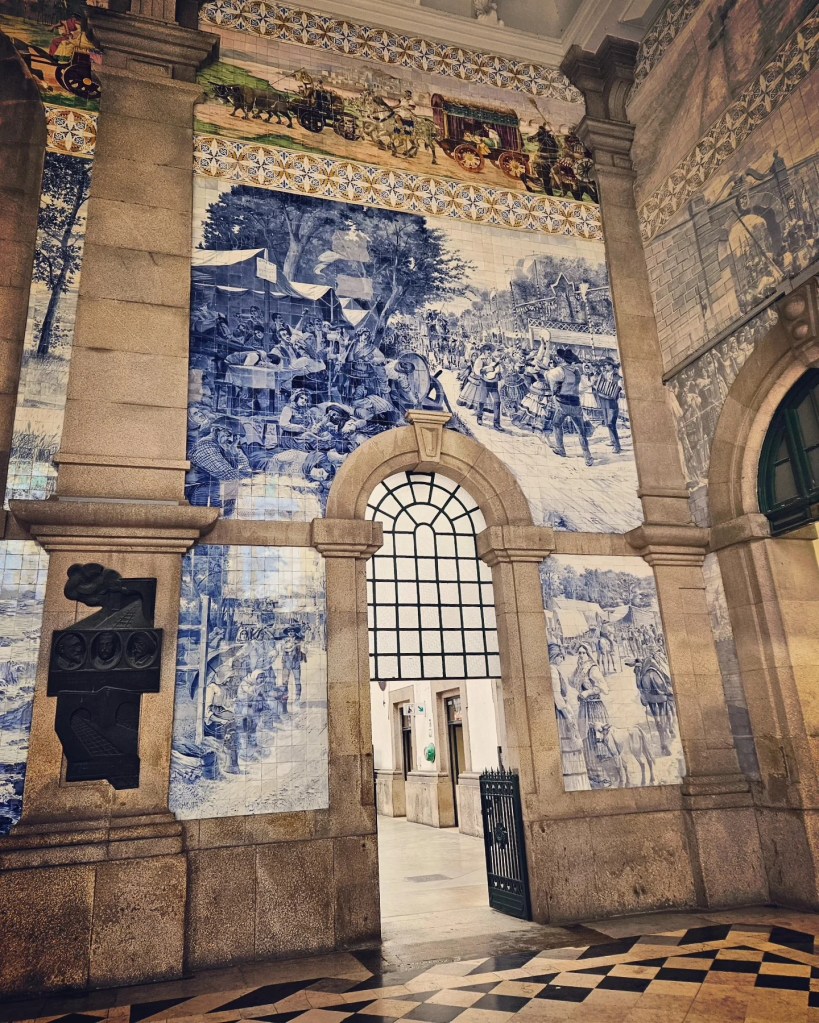 Massive blue and white azulejo tile mural inside São Bento train station in Porto, depicting historical scenes with people and carriages.
