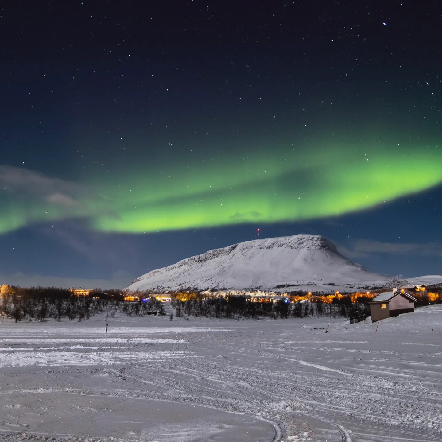 Northern Lights ripple above a snowy Finnish mountain town, the light painting a wave across the night sky.