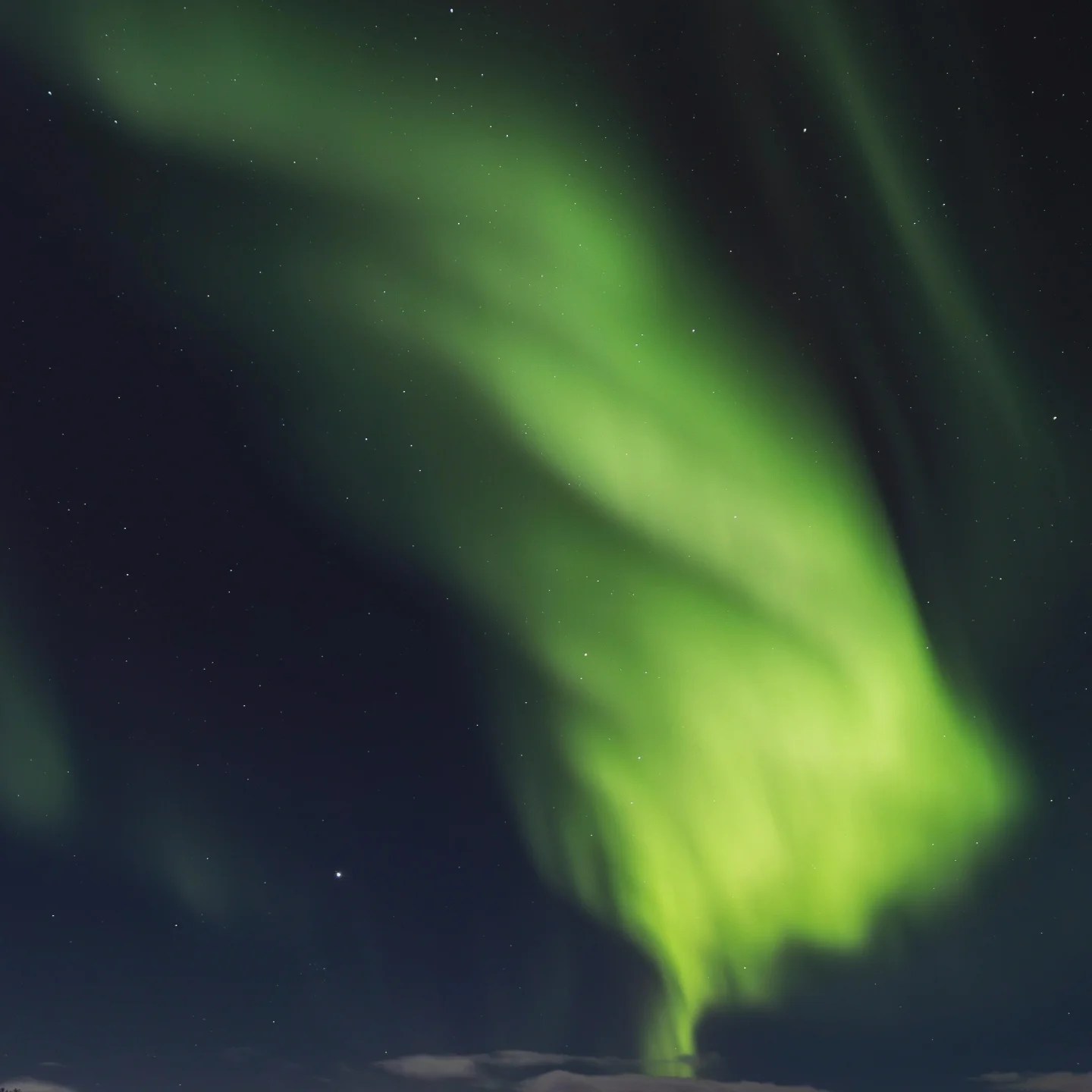 A close-up view of the Northern Lights forming a swirling column of green in the starry sky.