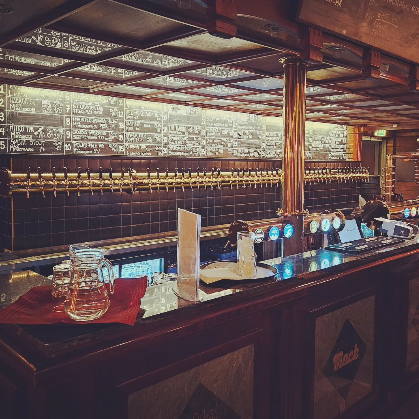 Long line of beer taps beneath a chalkboard wall listing craft beer selections inside Ølhallen pub.
