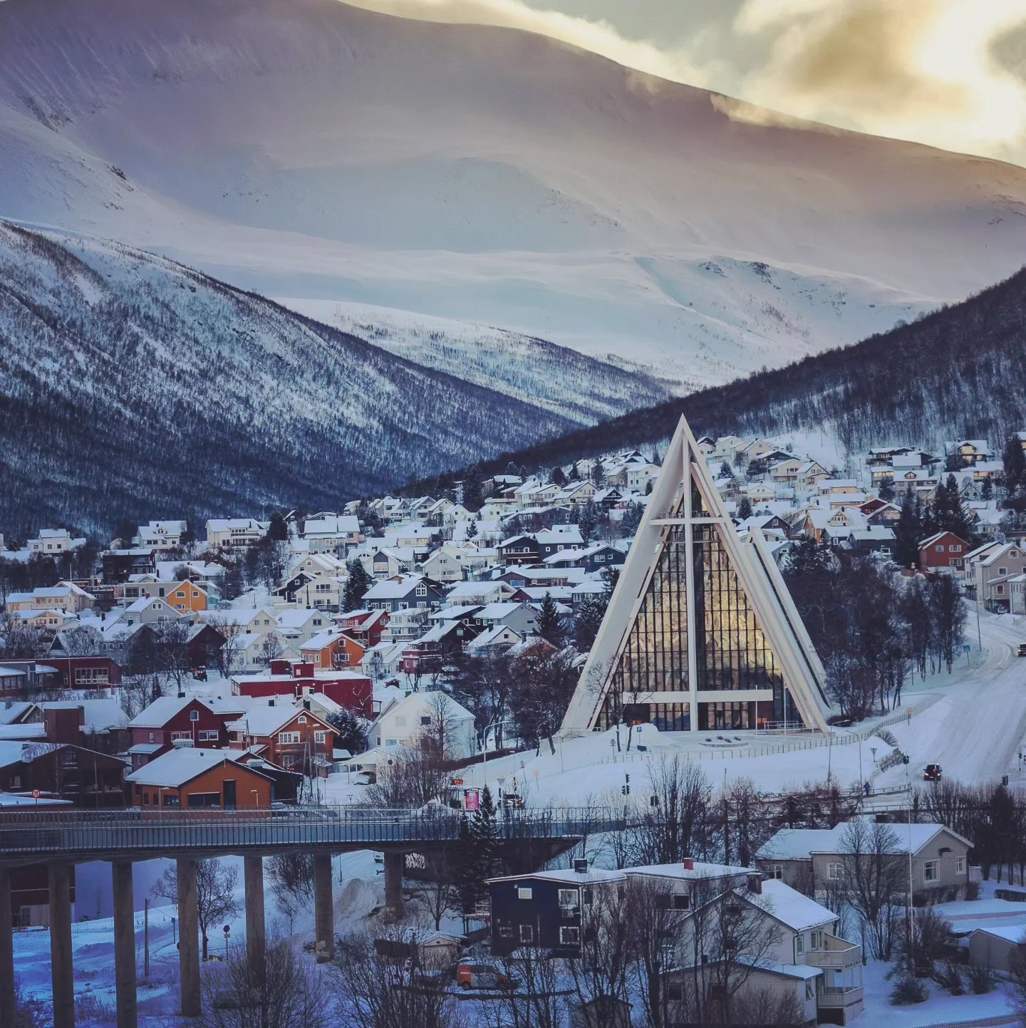 The Arctic Cathedral rises sharply above colorful snow-covered houses, backed by towering white mountains.
