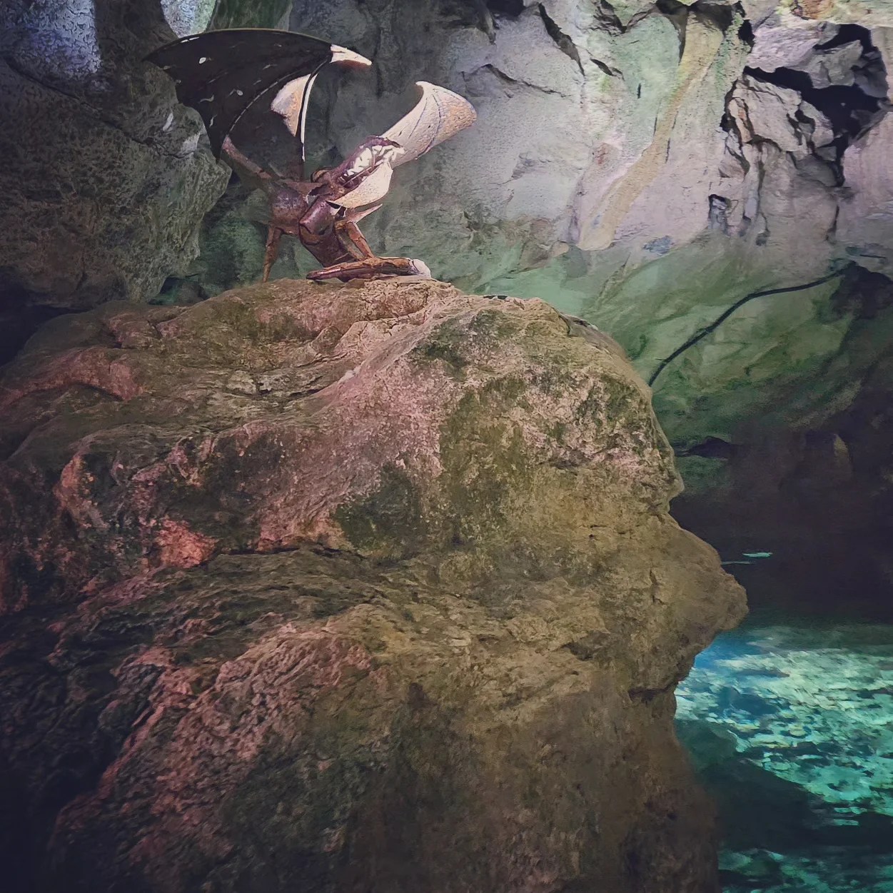 A metal dragon sculpture perched on a rock inside Wimsen Cave, Germany, with dramatic cave lighting highlighting the installation.
