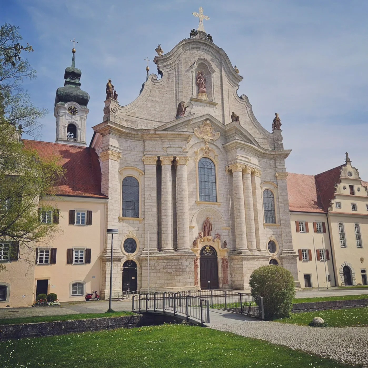 Baroque facade of Zwiefalten Abbey (Zwiefaltener Kloster), with grand columns, statues, and arched windows under a blue spring sky.