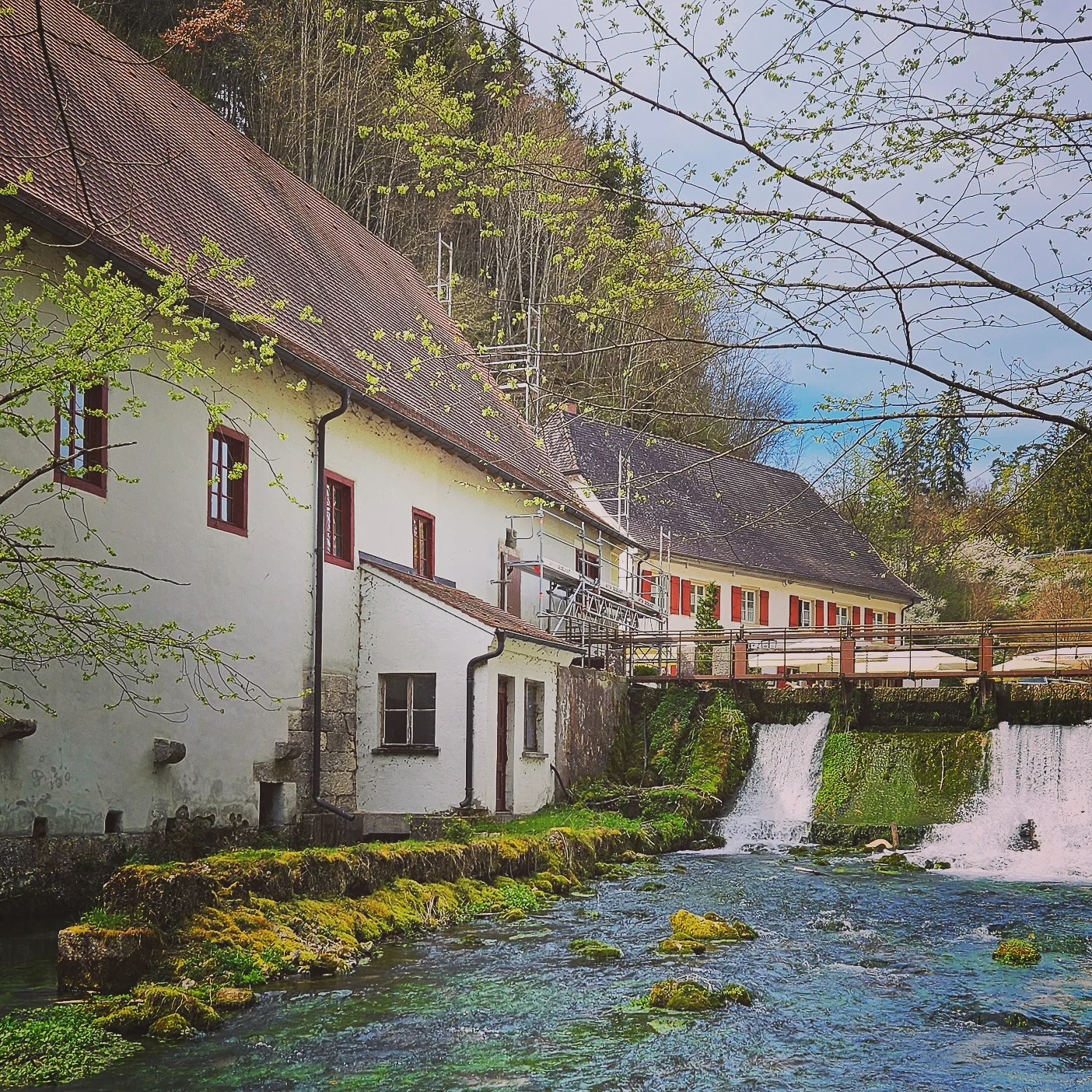 Historic Hasenmühle mill near Wimsen Cave, with moss-covered rocks and a small waterfall from the Zwiefalter Ach flowing in front.