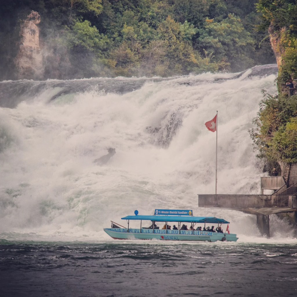 Blue sightseeing boat skimming past the main cataract of Rhine Falls.