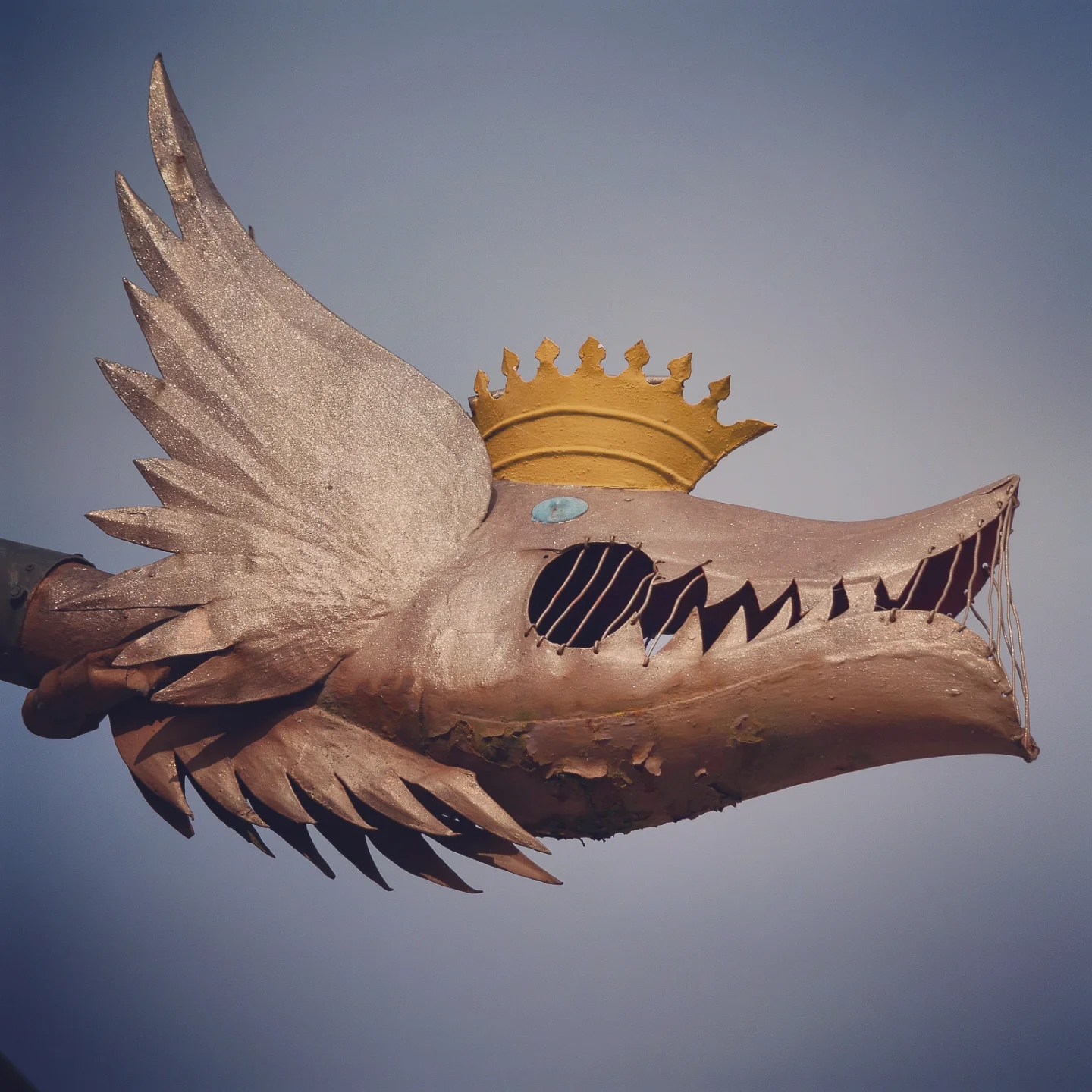 Close-up of a copper dragon rain-spout crowned with gold, set against a clear blue-grey sky.