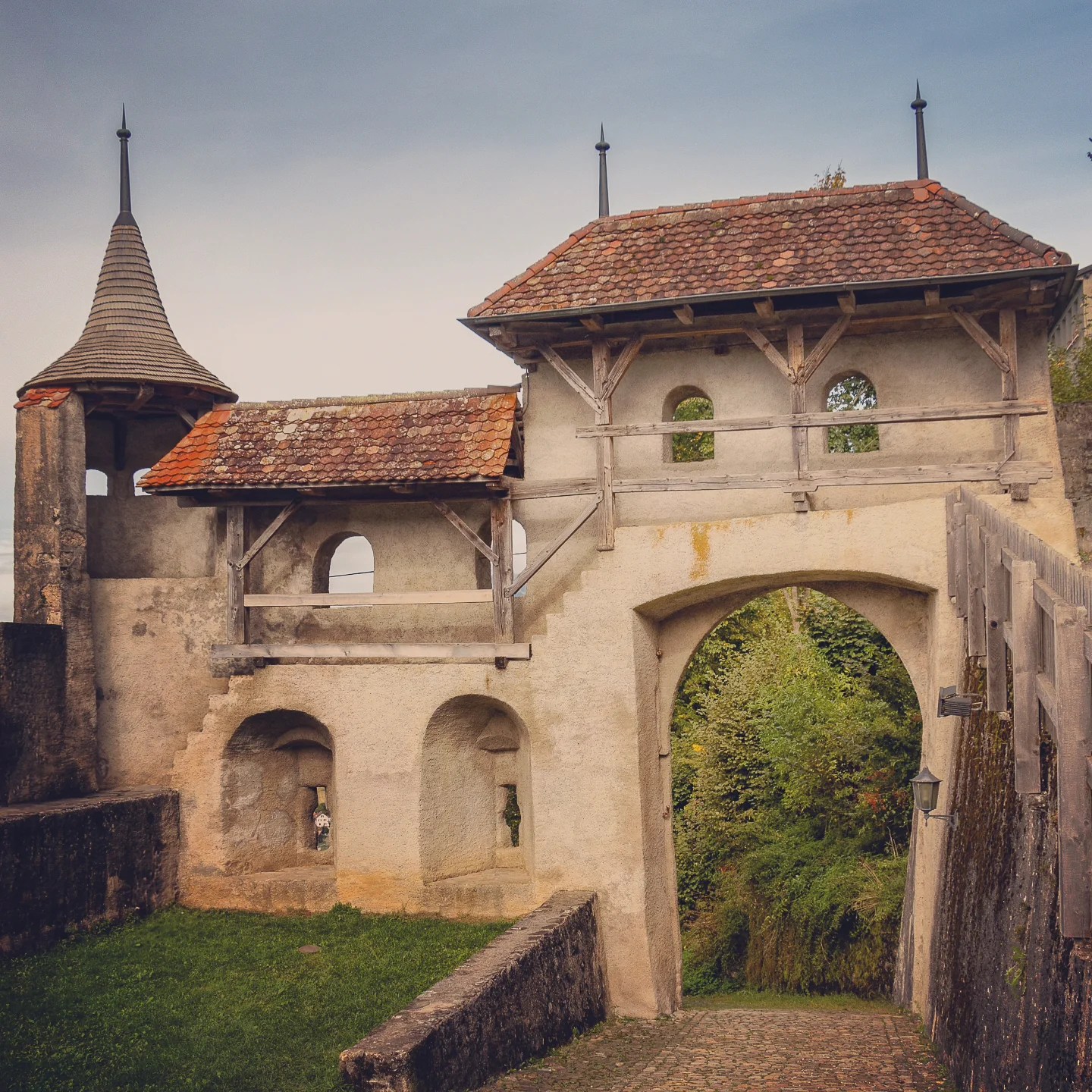 Stone archway with tiled watchtower and timber galleries—part of Gruyères’ fortified ramparts.