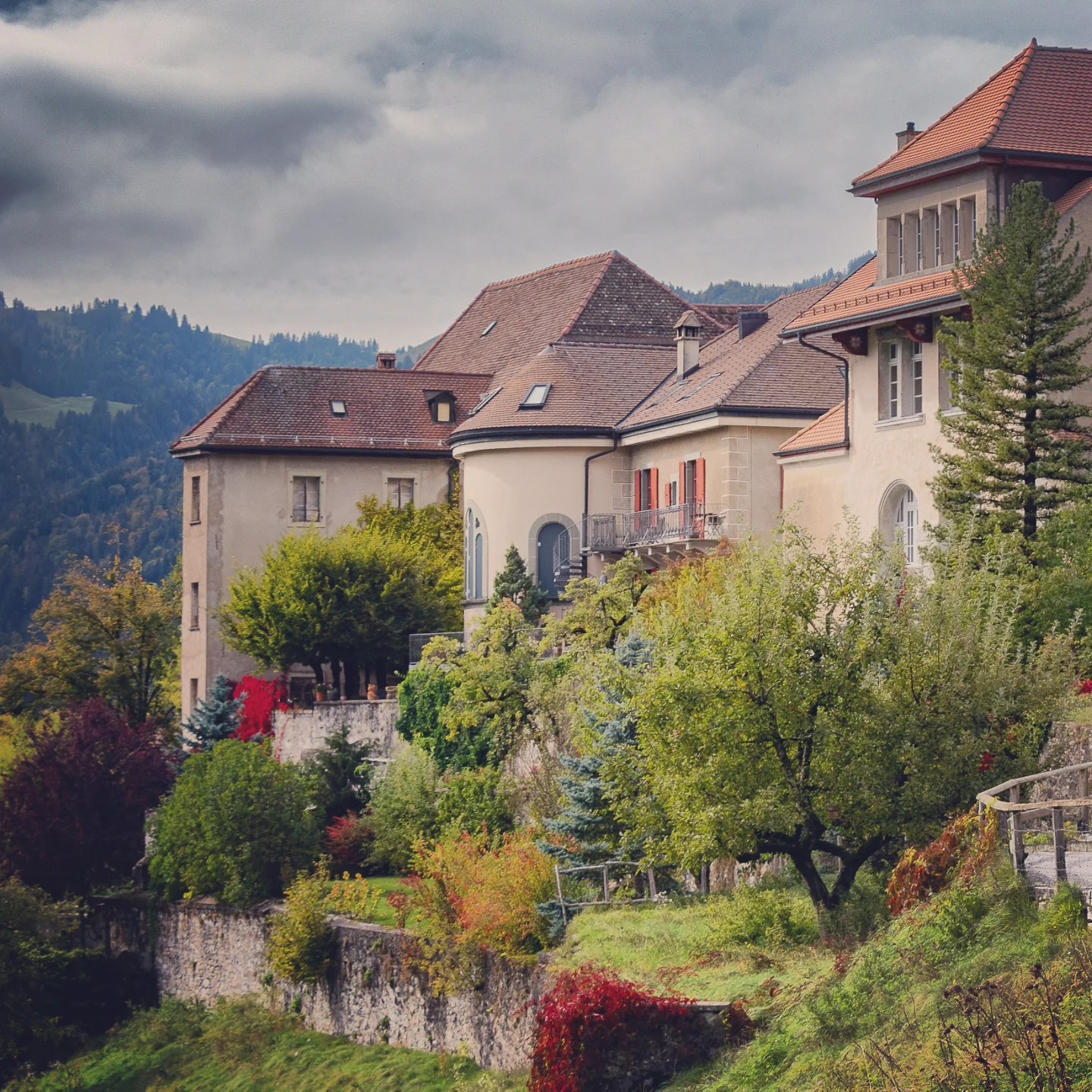 Row of hillside villas in Gruyères framed by autumn trees and moody clouds.