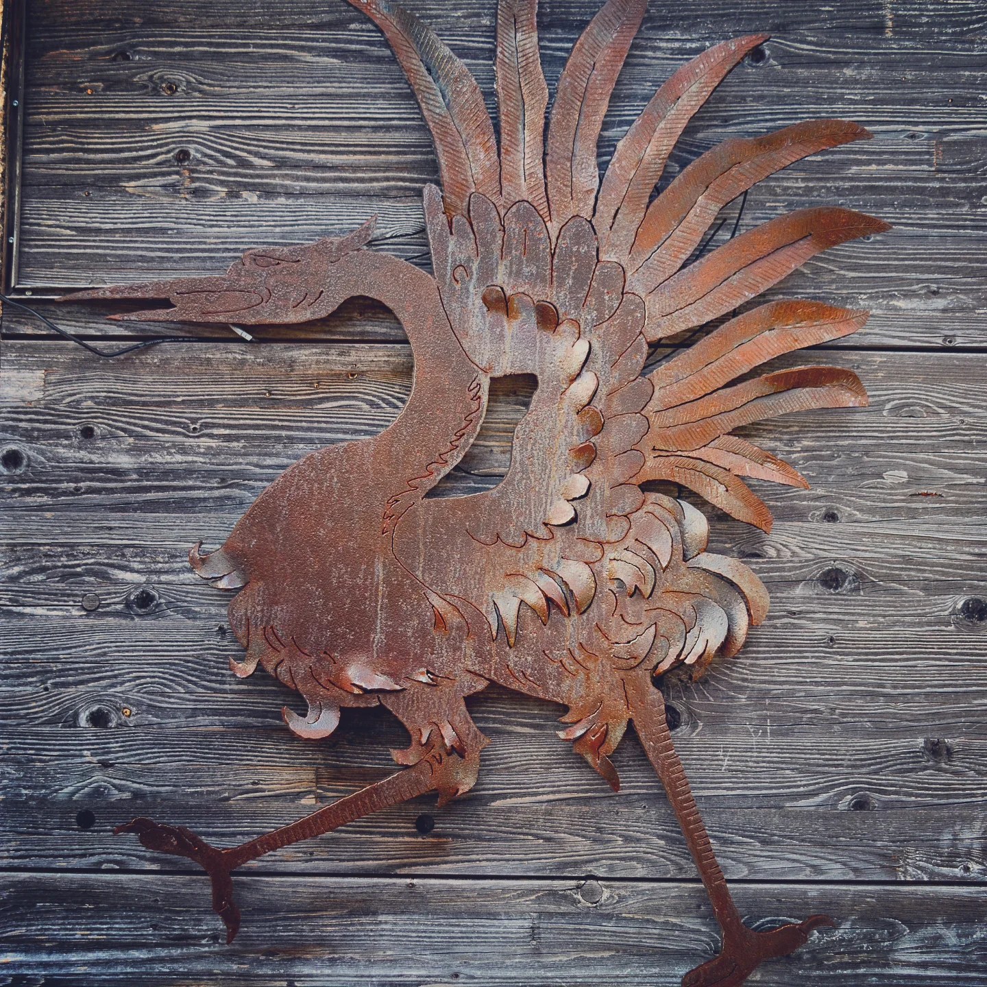 Rust-patinated metal crane emblem mounted on weather-worn wooden planks.