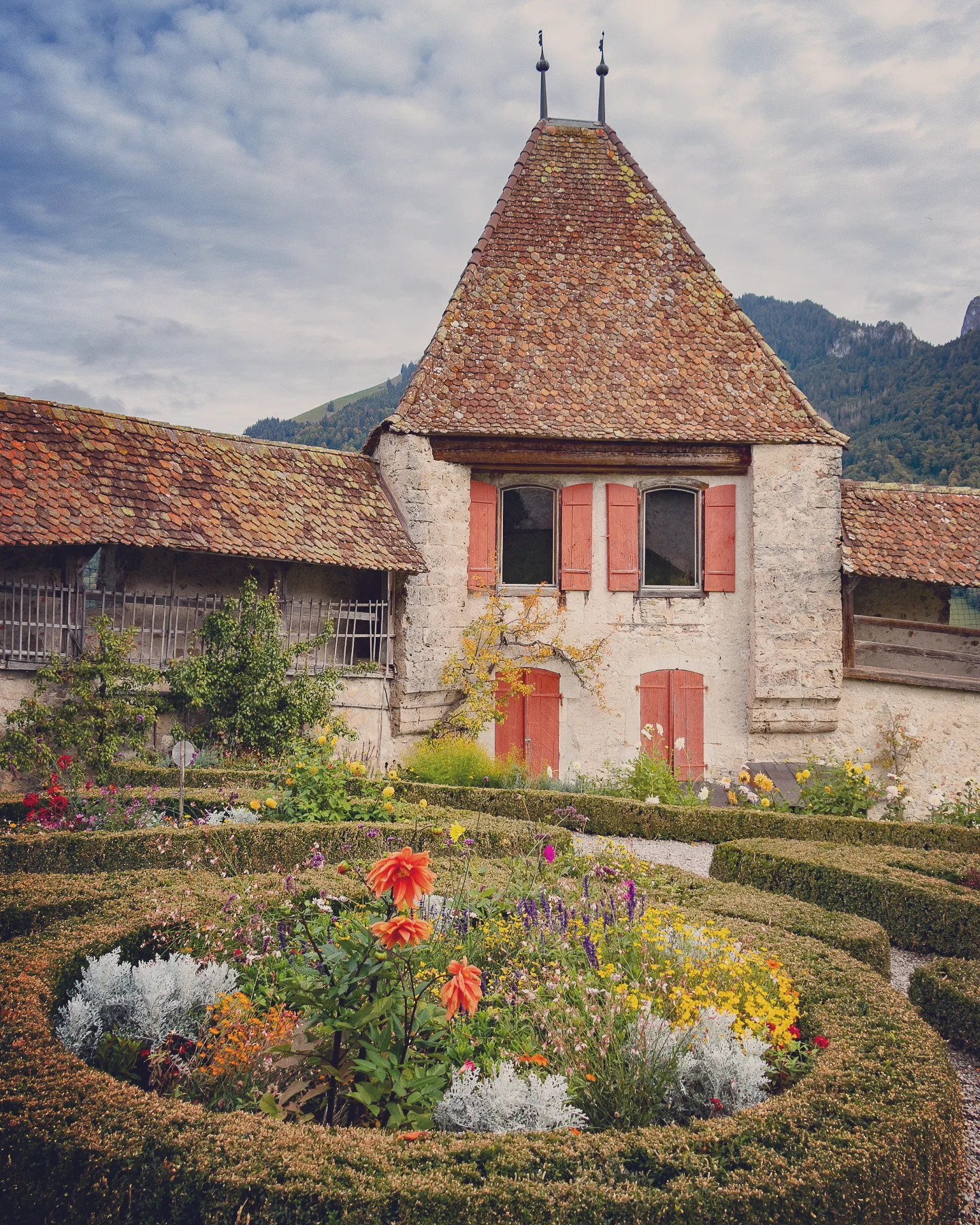 Box-hedge knot garden bursting with flowers outside a tiled-roof outbuilding of Gruyères Castle.