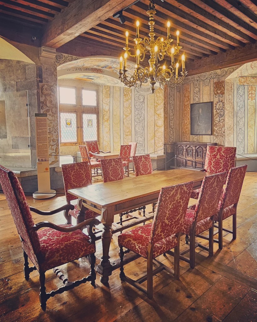 Wood-beam dining room with long oak table, red damask chairs and brass chandelier.