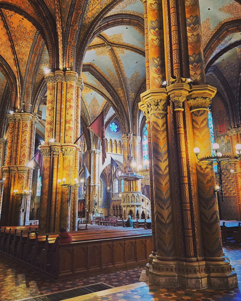 Interior of Matthias Church showing ornate painted columns, vaulted ceilings, and medieval-style décor.
