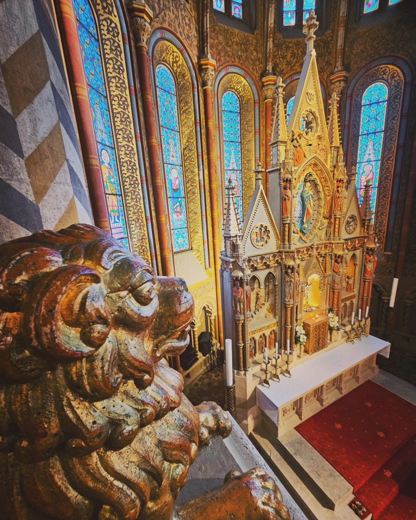 Close-up of a carved lion sculpture overlooking the altar of Matthias Church, with stained glass in the background.