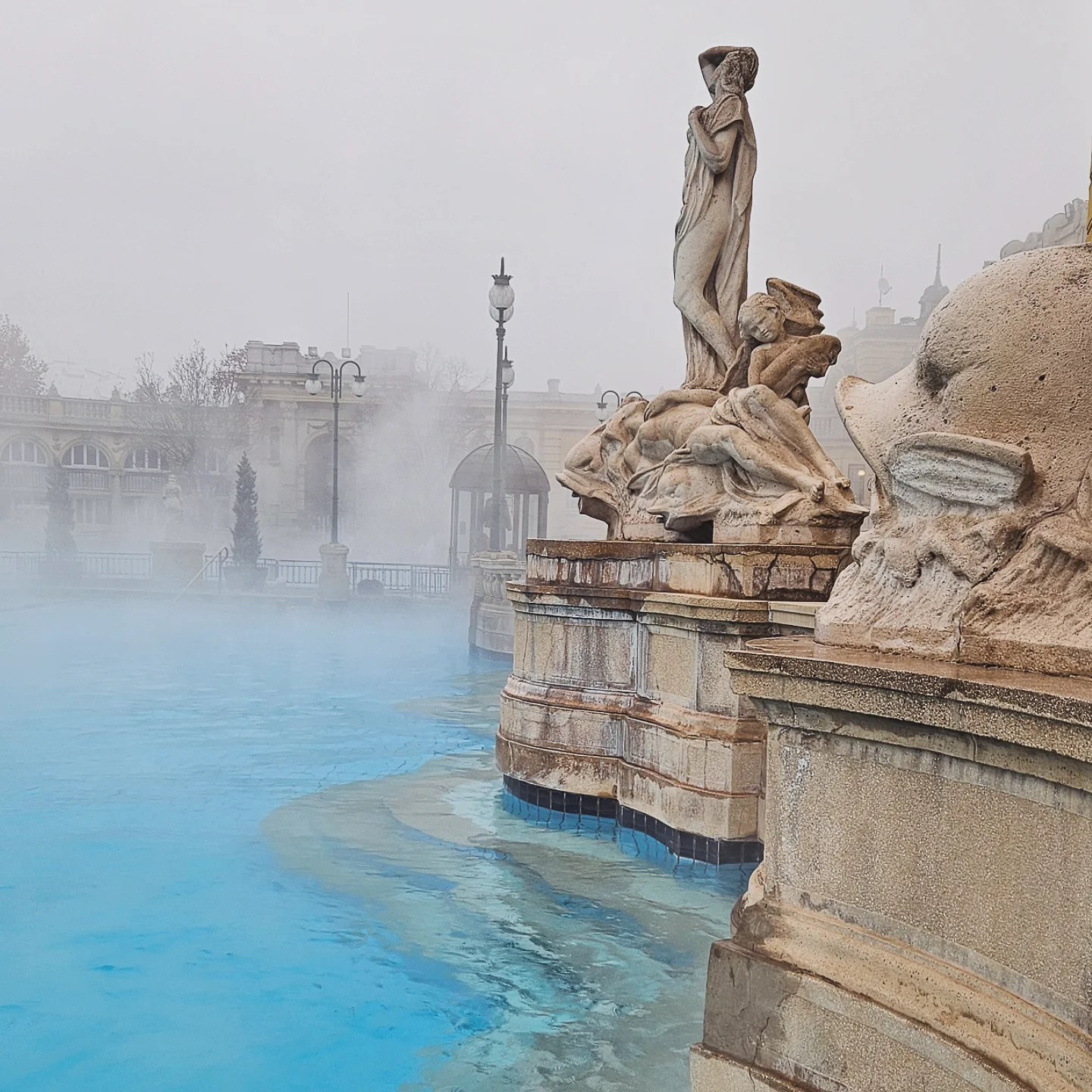 Steamy thermal pool at Széchenyi Thermal Bath with classical statues and deep blue water.