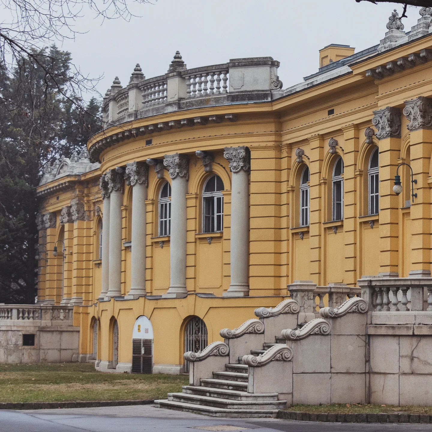 Exterior of a Baroque yellow bathhouse with tall columns, arched windows, and decorative balustrades