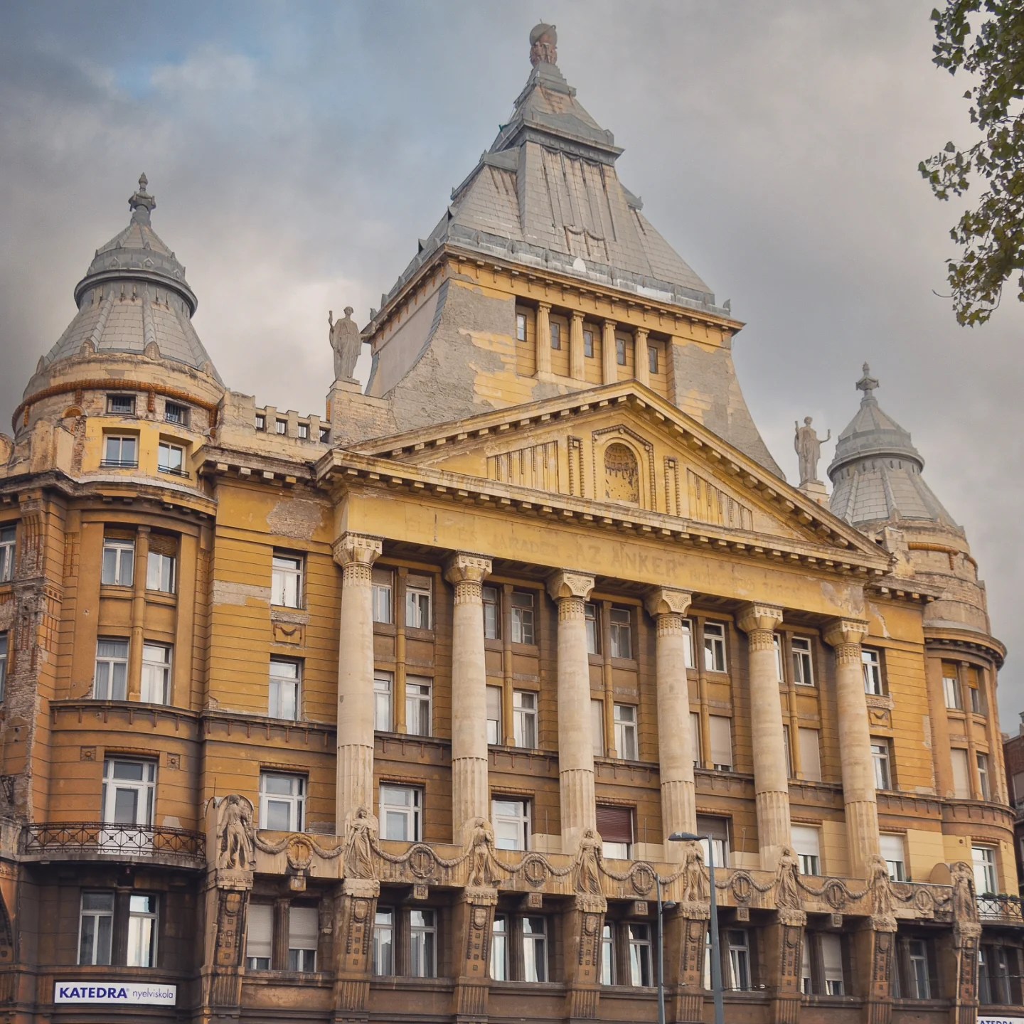 Yellow historic building with columns and statues - Anker Palace in Budapest.