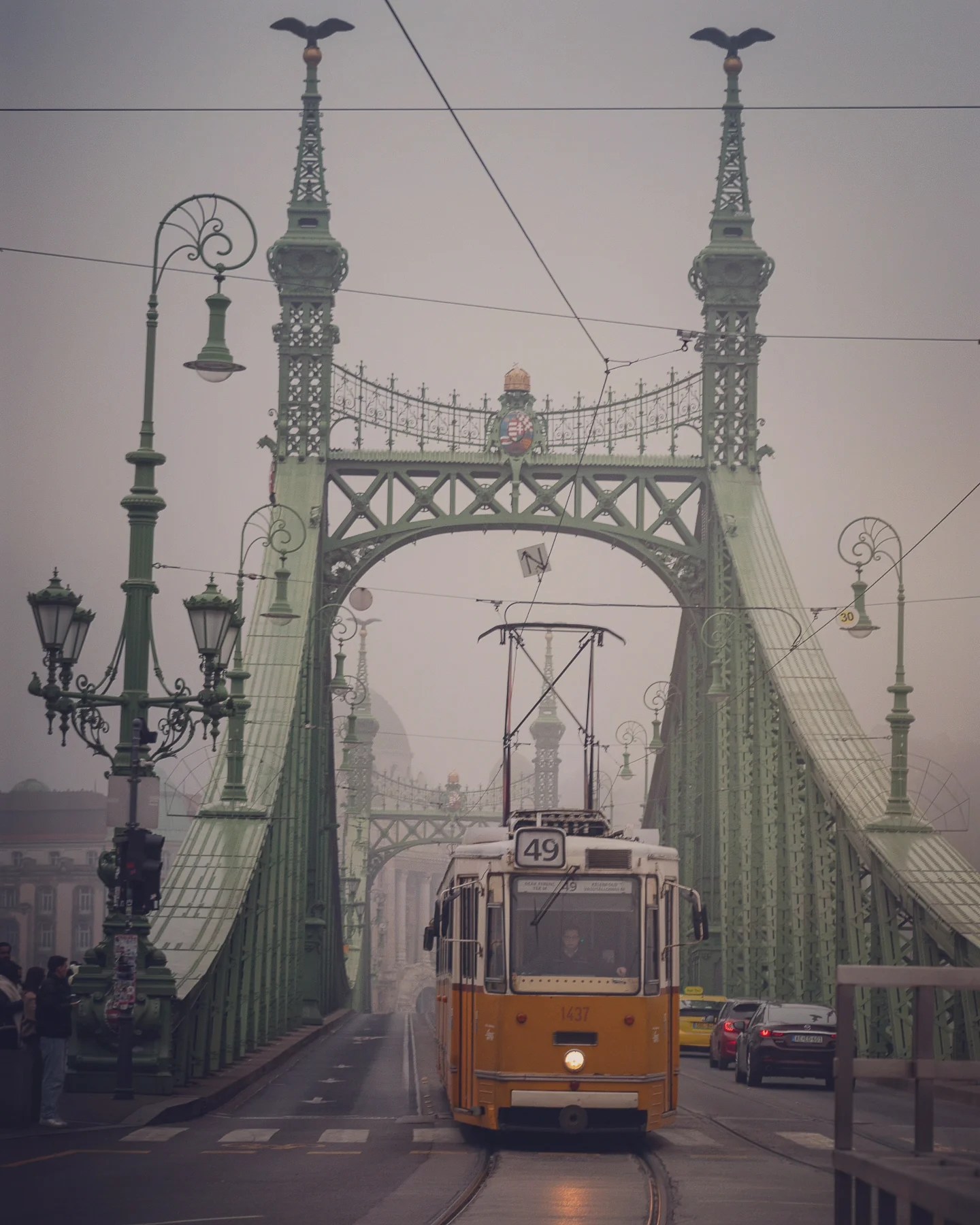 Classic yellow tram 49 crossing Liberty Bridge on a foggy day in Budapest.