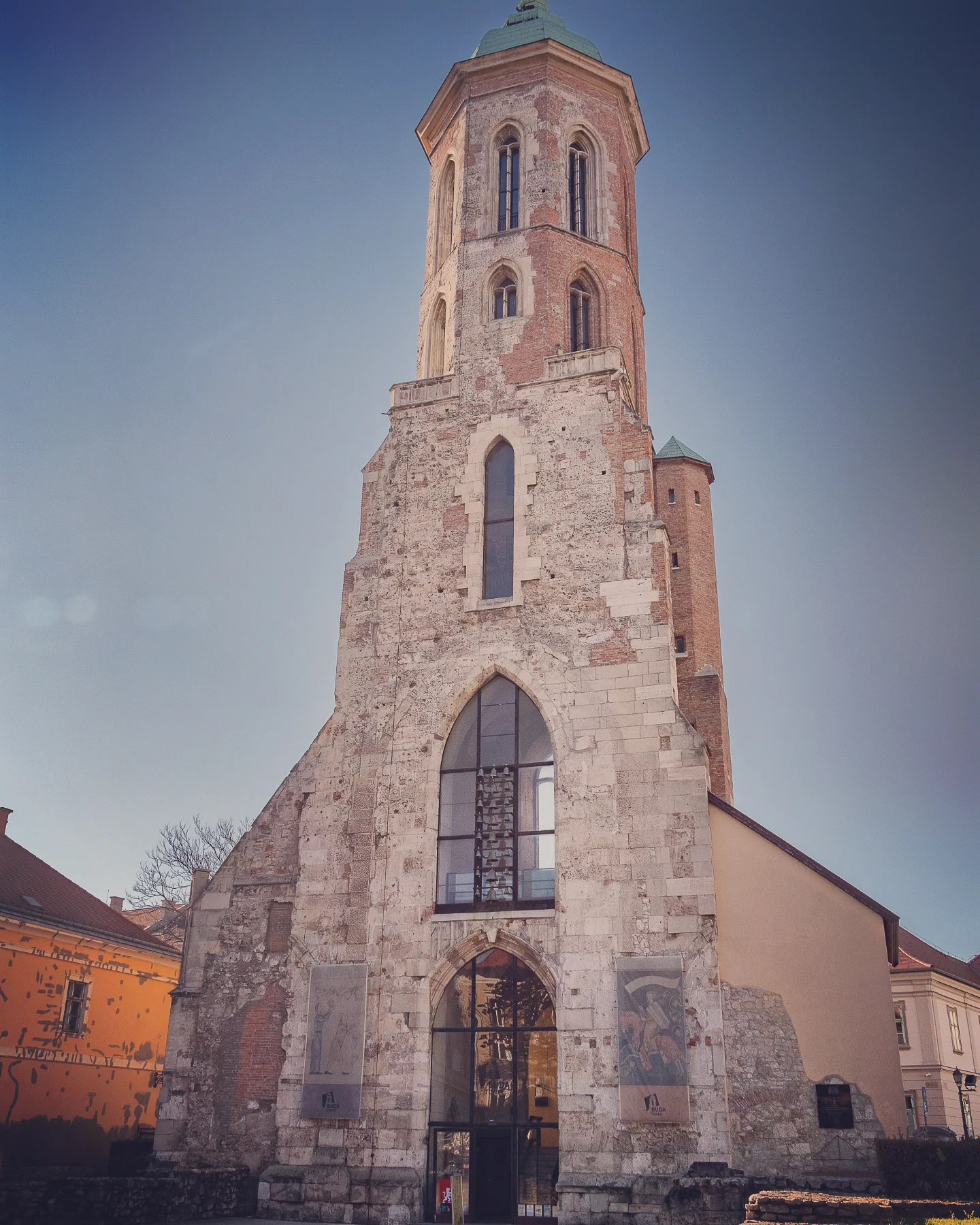 Ruins of a tall brick and stone church tower with gothic-style arches in Budapest.