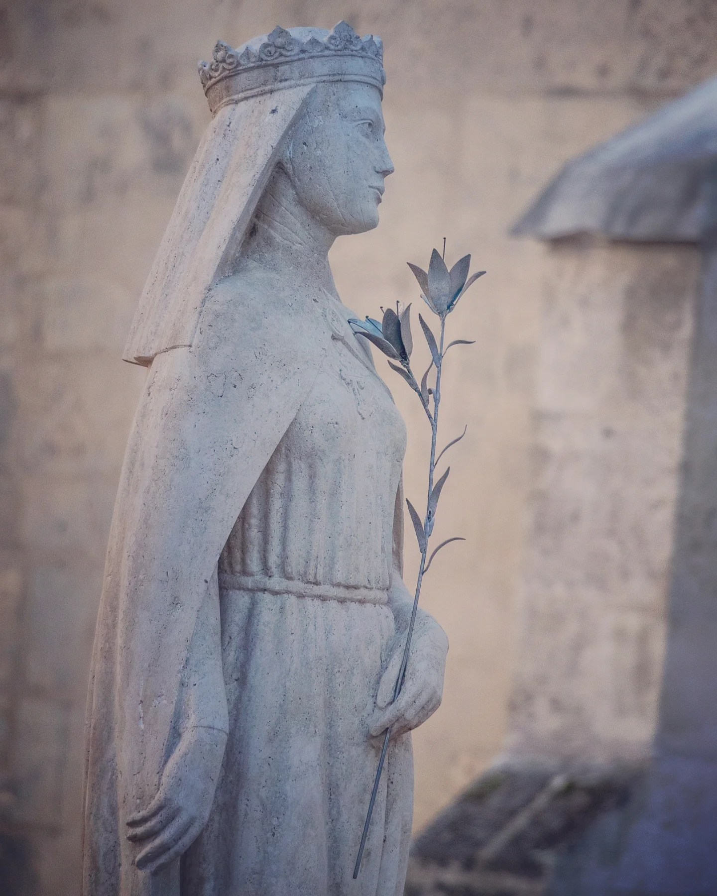 Stone statue of a crowned woman holding flowers, with a serene expression.