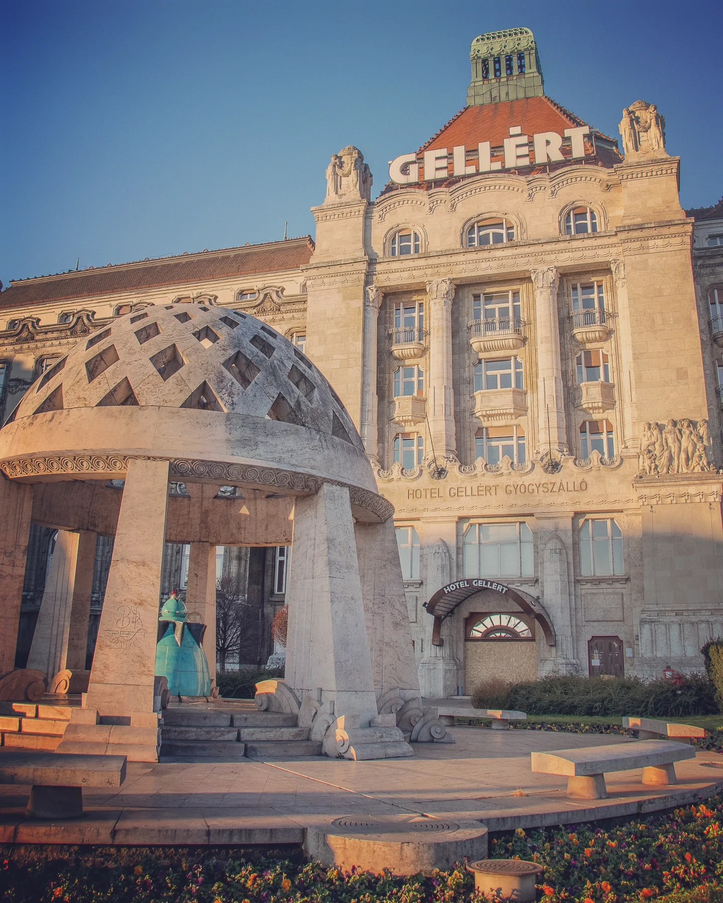 Front view of Hotel Gellért in Budapest with art deco-style dome statue in the foreground.