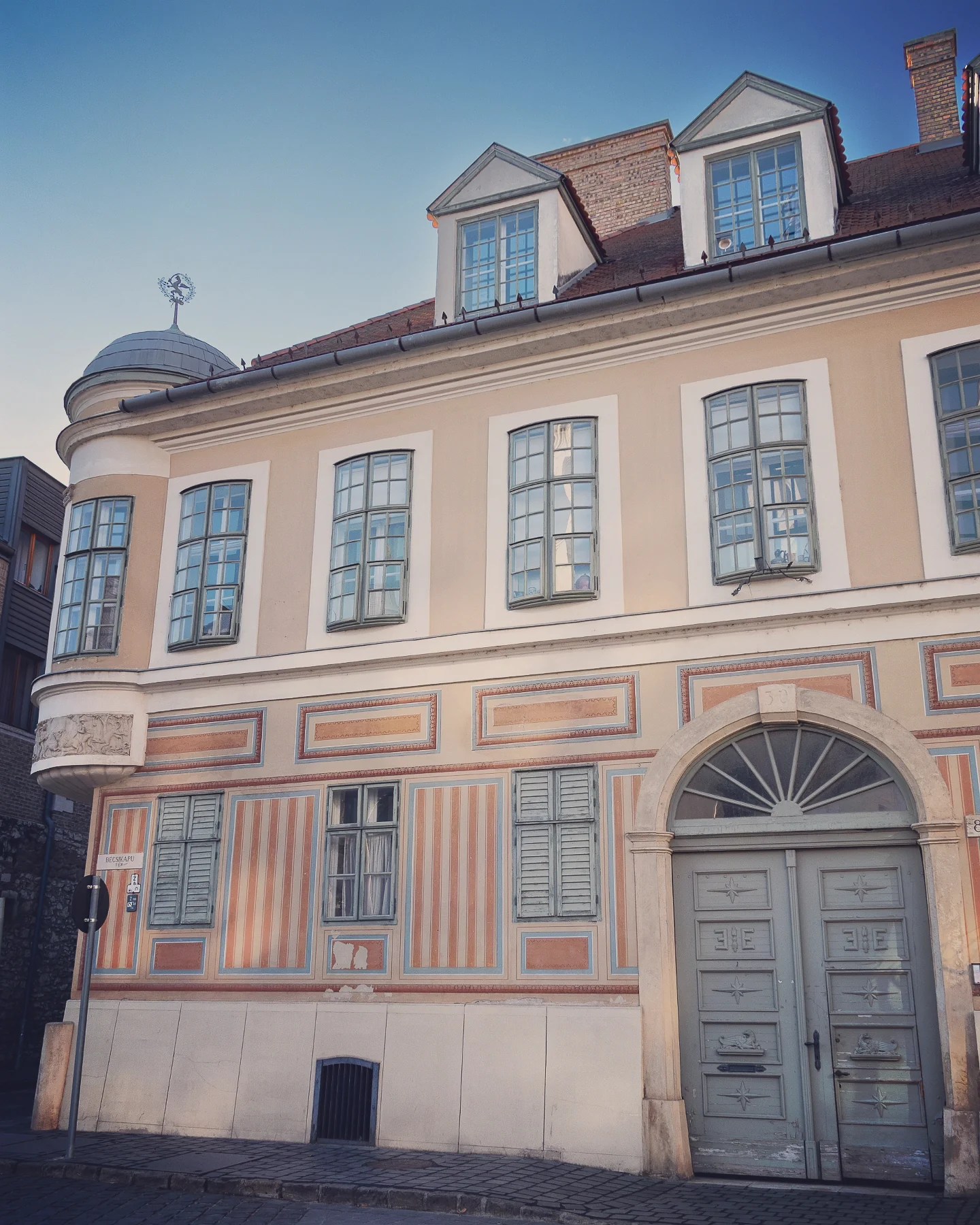 Historic pastel-striped building with blue shutters and arched doorway in Budapest.