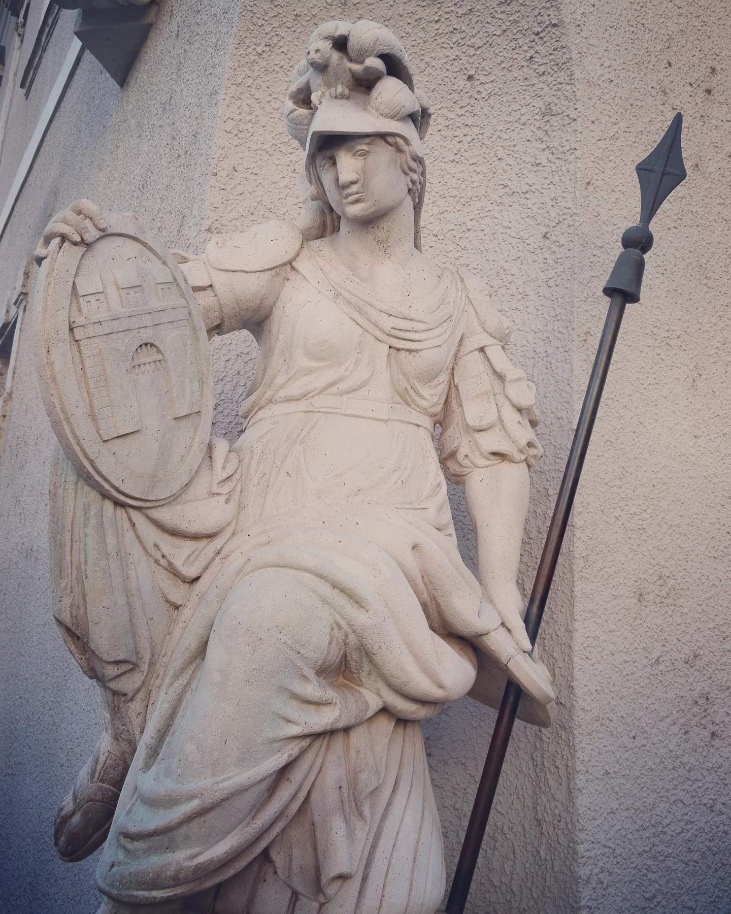 White stone statue of a female warrior holding a spear and shield with a castle emblem.