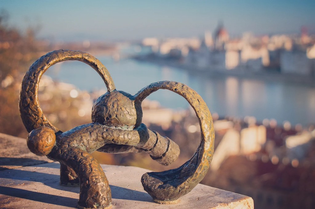 Small bronze rabbit statue with exaggerated ears overlooking the Danube and blurred view of the Parliament Building.