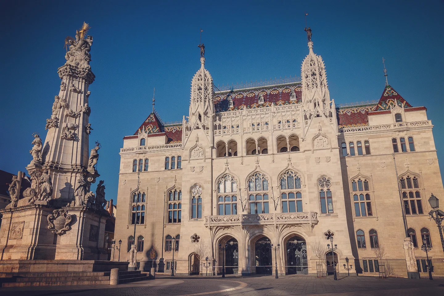 Neo-Gothic façade of Hungary’s Ministry of Finance next to the ornate Holy Trinity Column in Budapest’s Castle District.