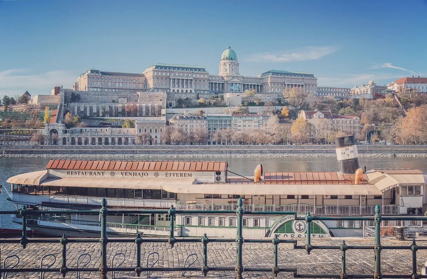 Moored restaurant boat on the Danube with a clear view of Buda Castle and its dome rising above the cityscape.