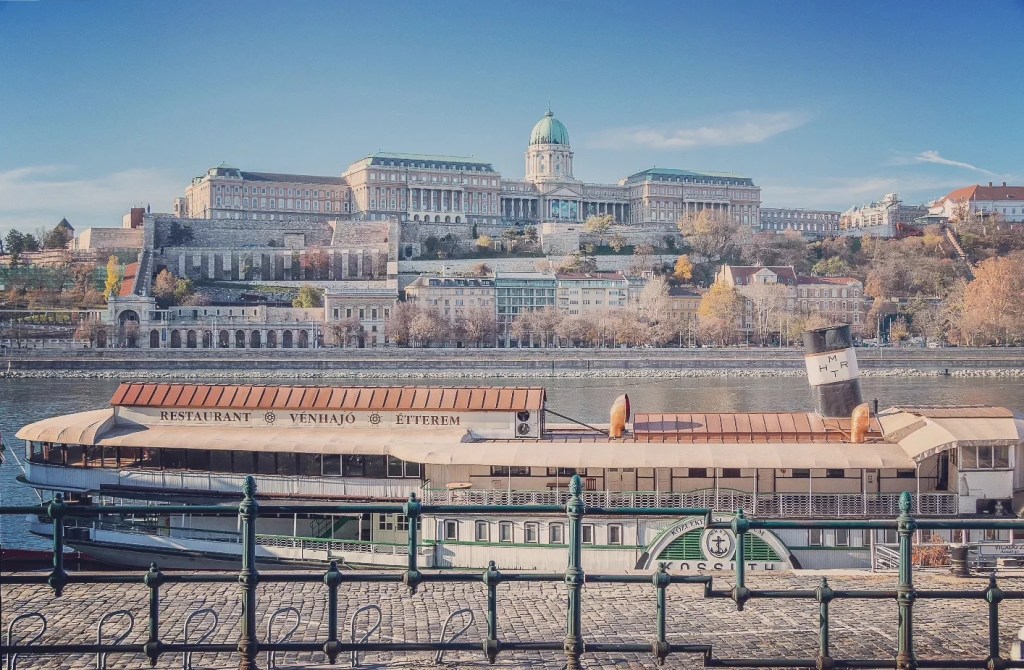 Moored restaurant boat on the Danube with a clear view of Buda Castle and its dome rising above the cityscape.