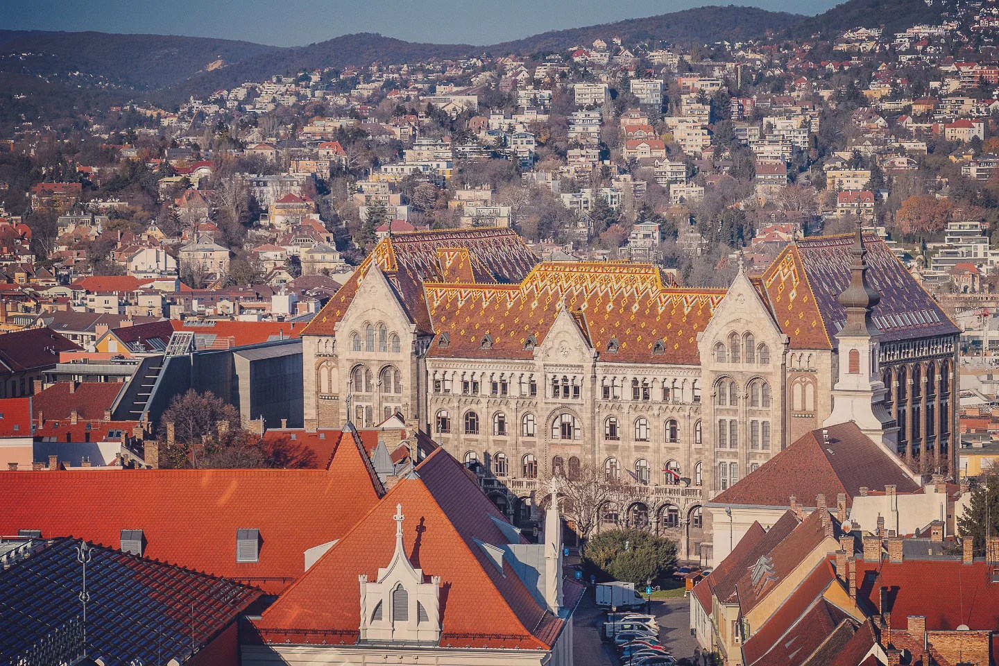View of the National Archives of Hungary with its colorful tiled roof, surrounded by rooftops and hills in Budapest.