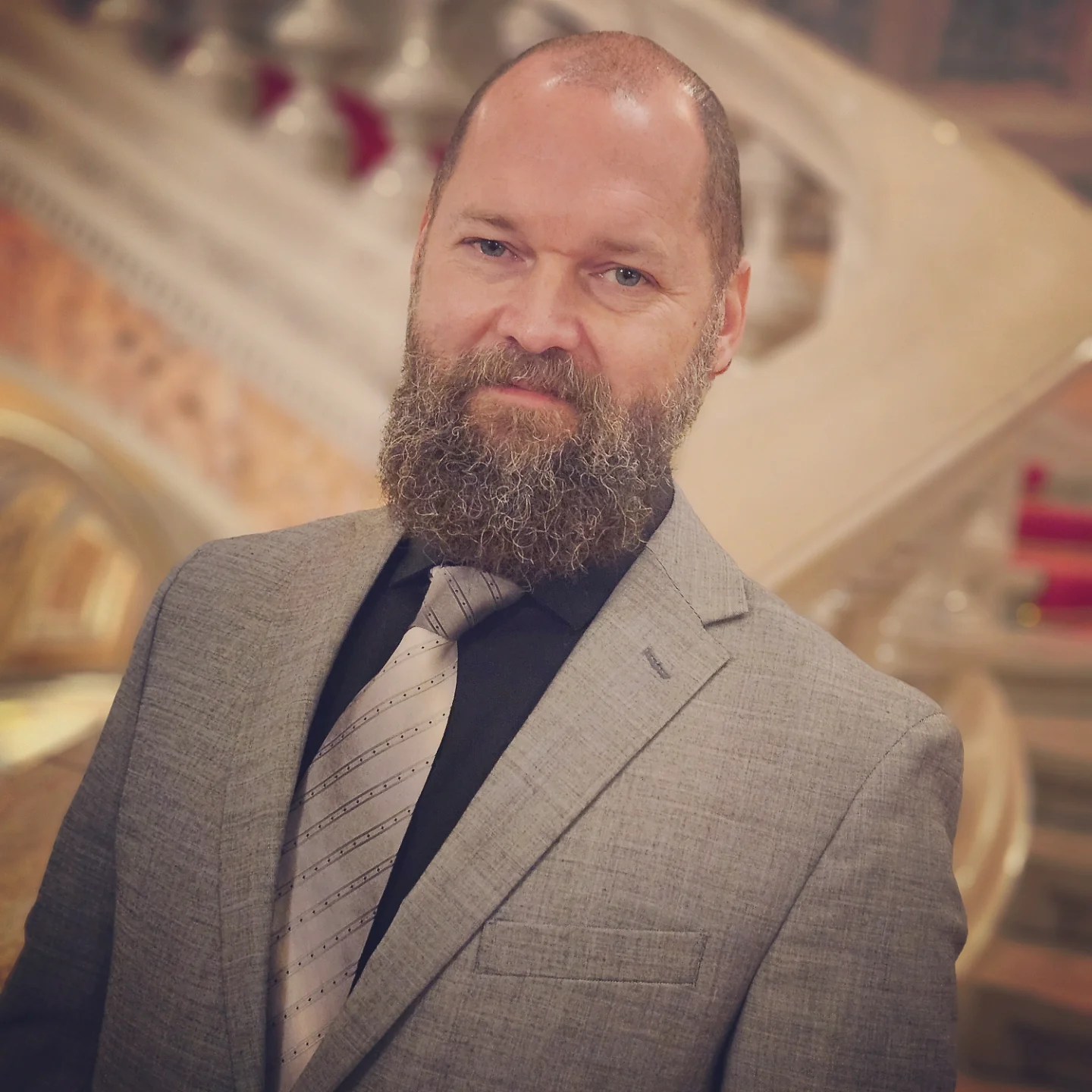 Man in a gray suit with a full beard standing inside the Hungarian State Opera House.