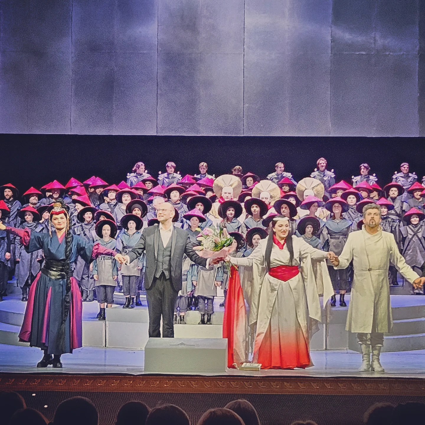 Curtain call at the opera with lead performers and full cast standing on stage.
