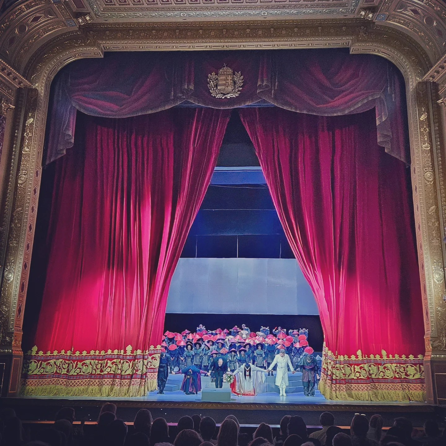 Cast of the opera bowing in front of an open red curtain during final applause.