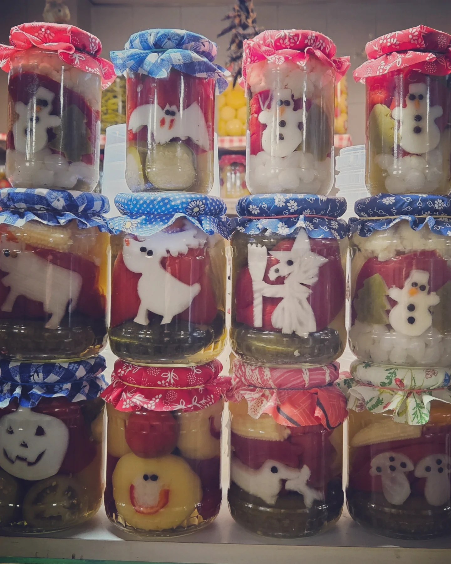 Jars of pickled vegetables arranged in rows, decorated with whimsical faces and shapes like snowmen, ghosts, and bats.