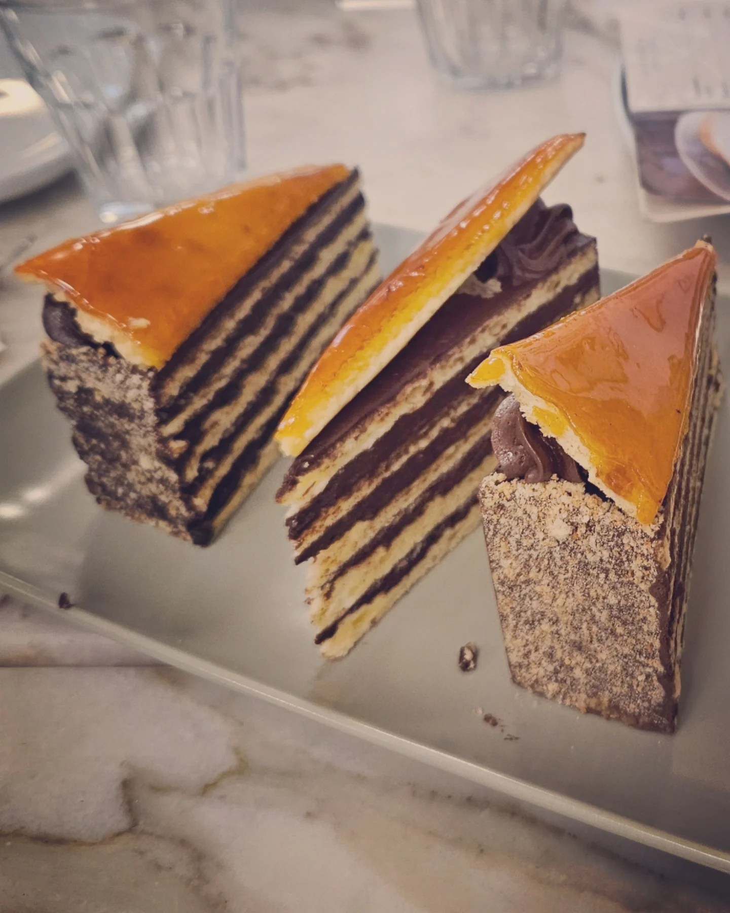 Three slices of Dobos Torte with shiny caramel tops and chocolate filling on a marble table.