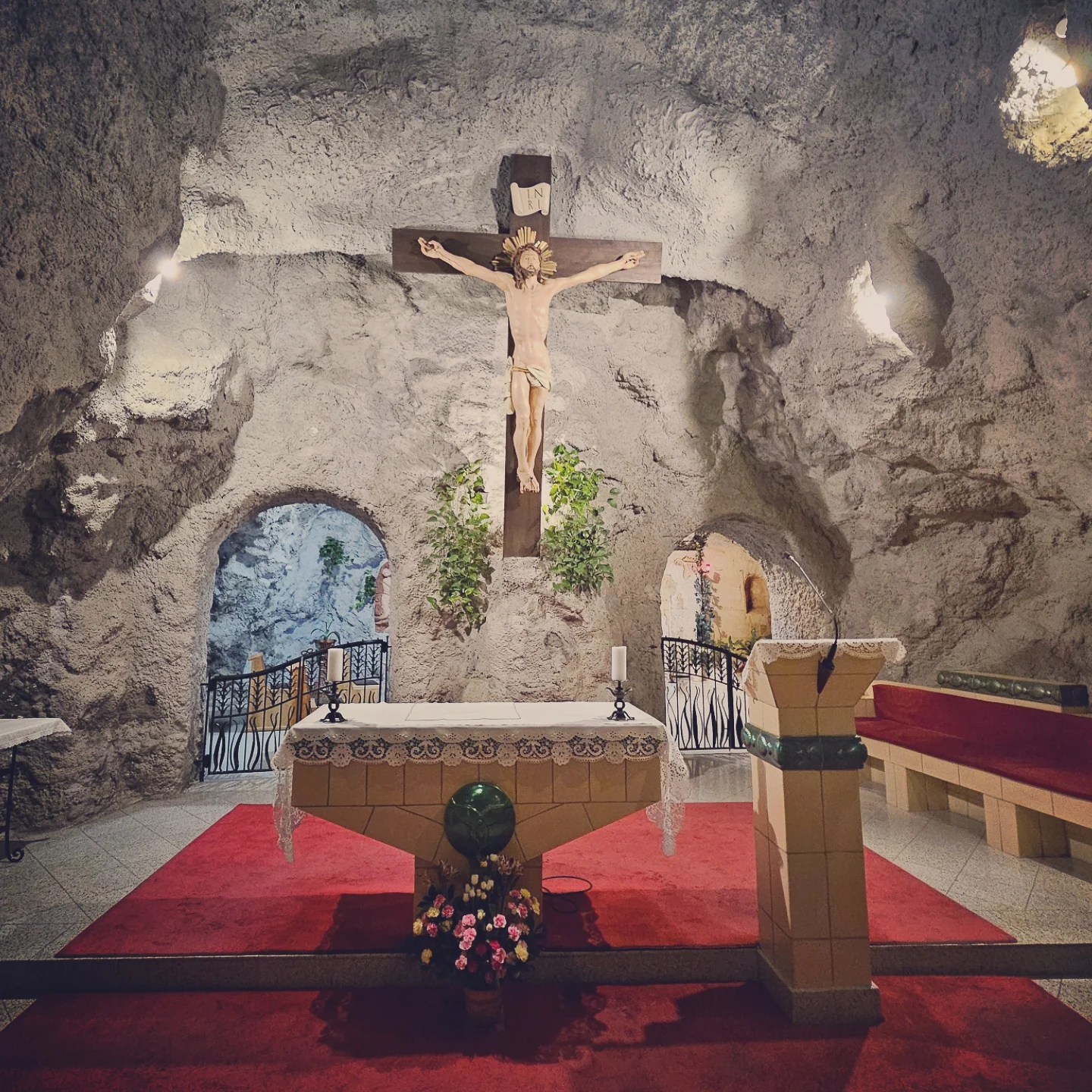 Stone interior of the Cave Church with an altar, crucifix, and red carpet.