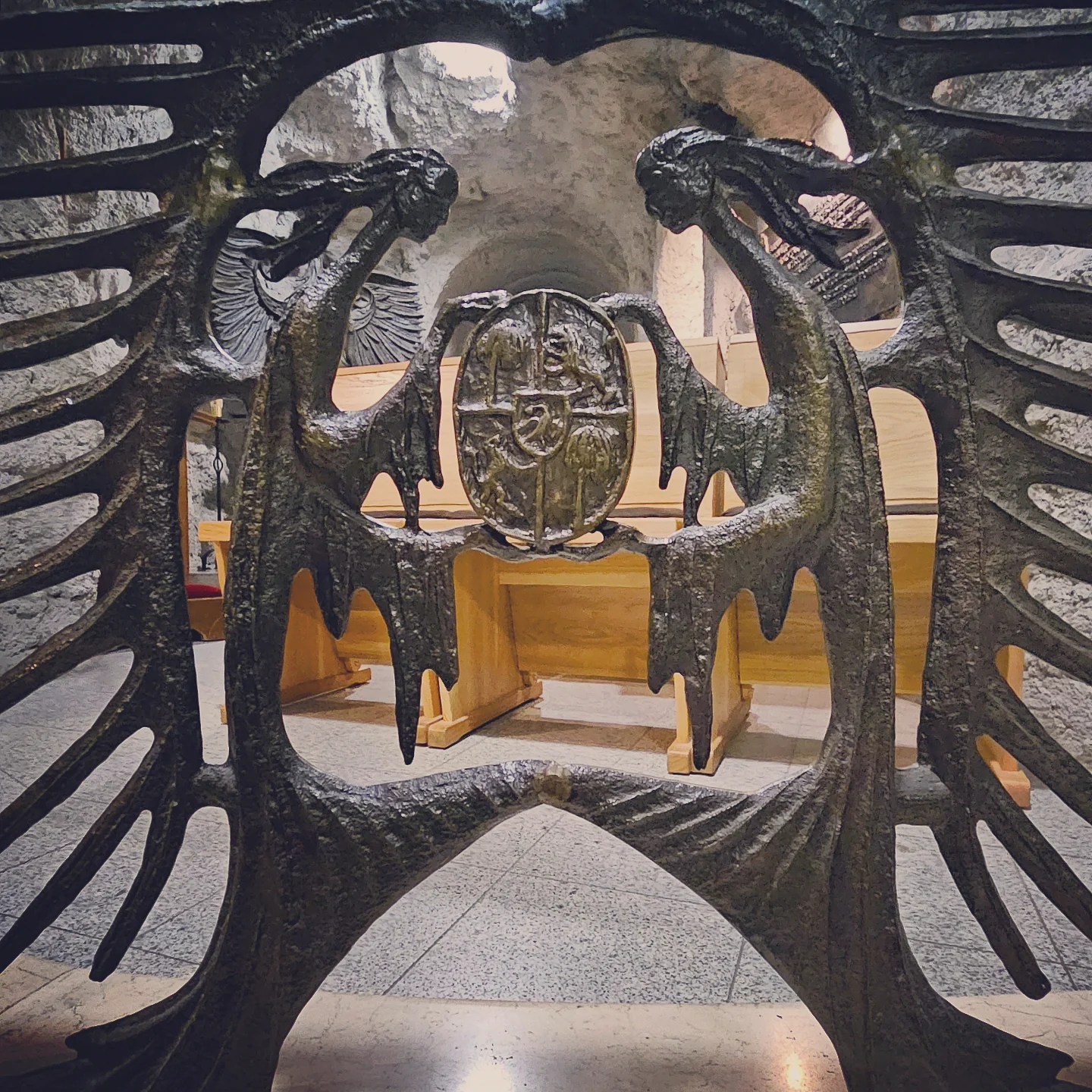 Close-up of a dramatic wrought-iron gate featuring twin women figures and a crest inside the Gellért Hill Cave Church in Budapest.
