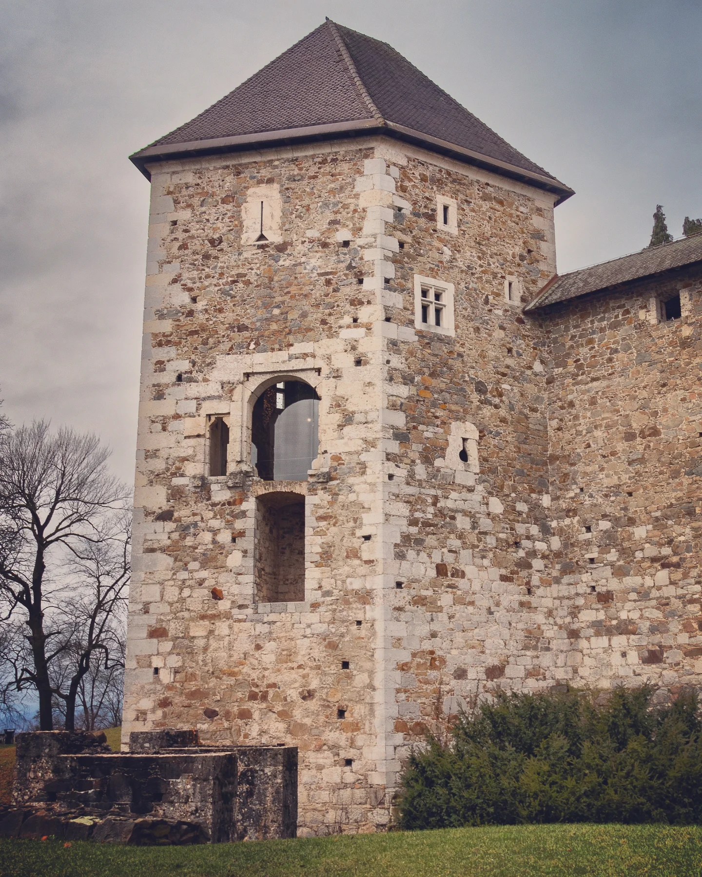 A tall, medieval stone watchtower with arched windows and a pointed roof, part of Ljubljana Castle, standing against a wintry, overcast backdrop.