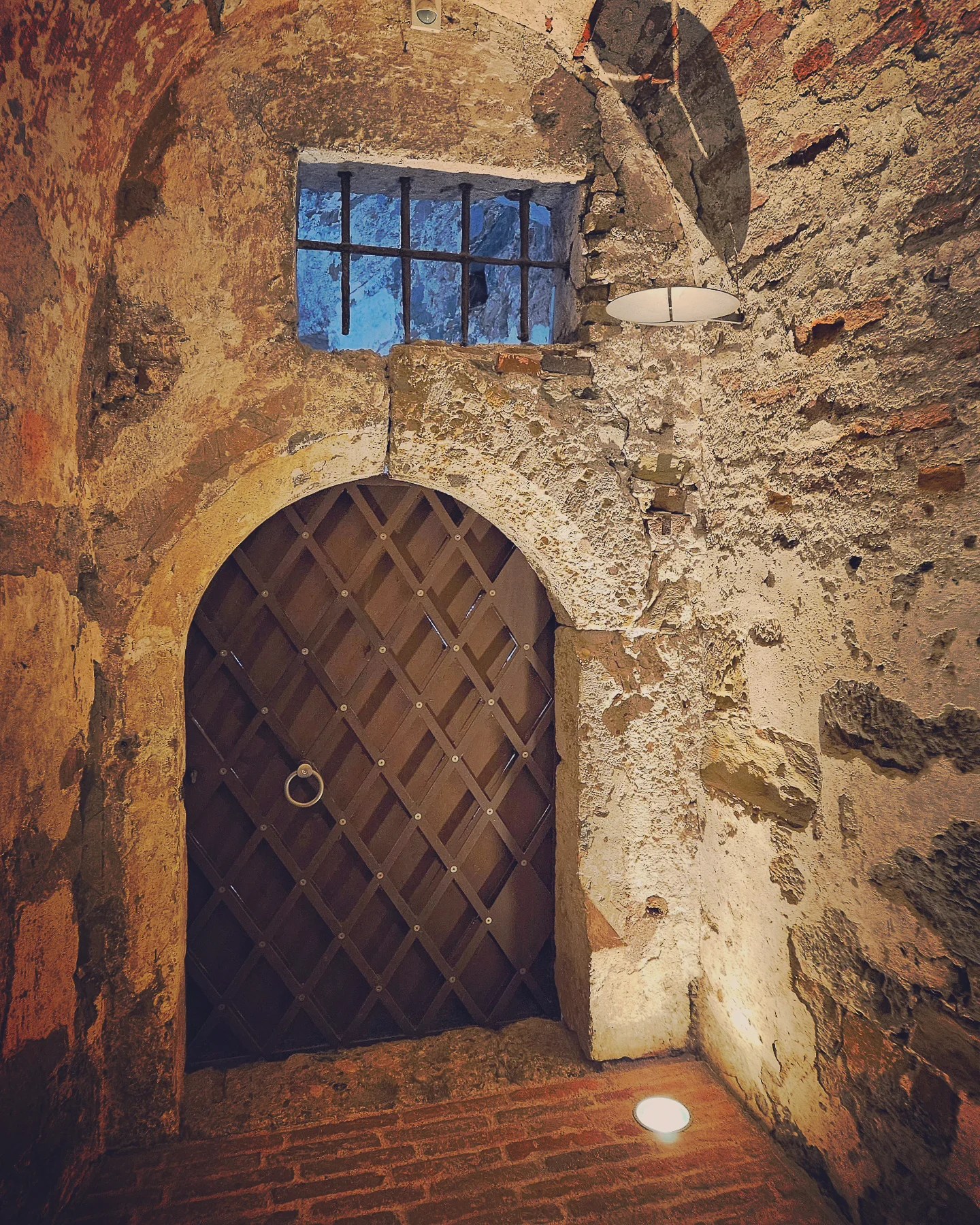 A heavy wooden door with metal grating and a barred window set within the ancient stone walls of Ljubljana Castle’s dungeon.